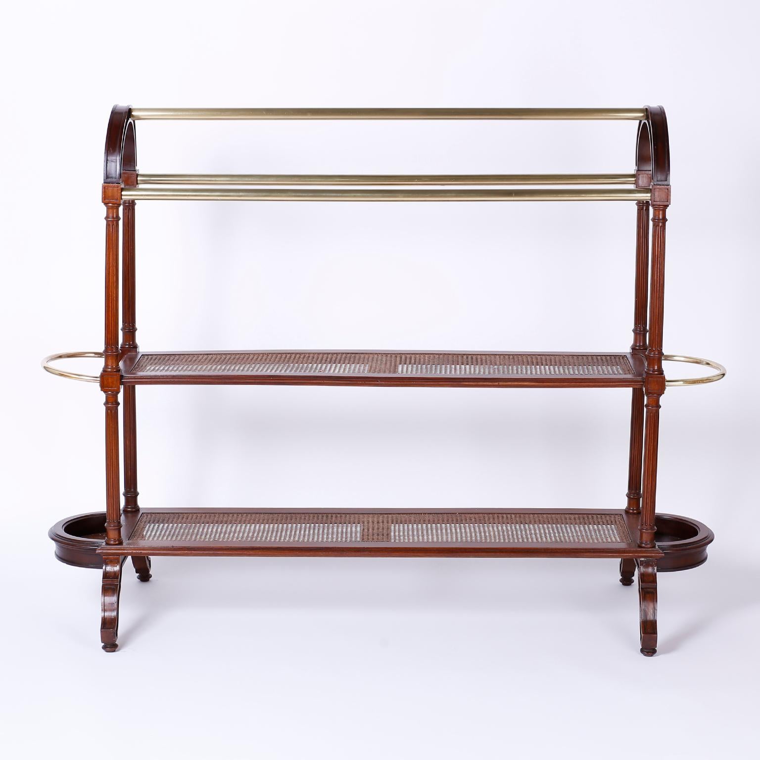 Antique British colonial mahogany quilt rack with an elegant form and plenty of storage. Having three brass poles over two canned shelves, side service racks and fluted supports, all over scrolled legs with button feet. The perfect combination of