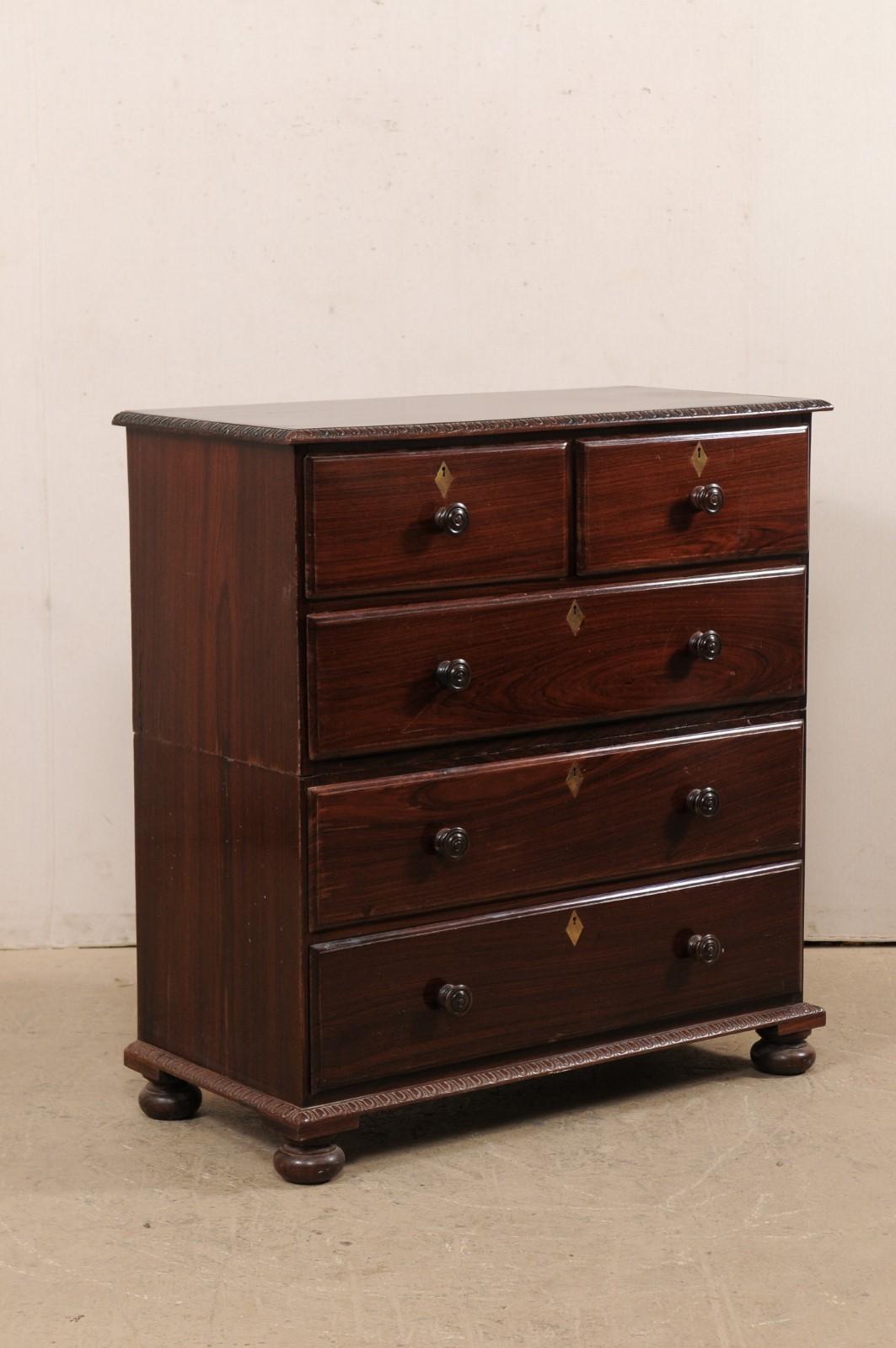 A British Colonial rosewood chest of drawers from the early 20th century. This antique chest from India is made of rosewood, giving it a beautifully rich presence. Egg-and-dart trim carvings accentuate the top lip and lower skirt. The cabinet houses