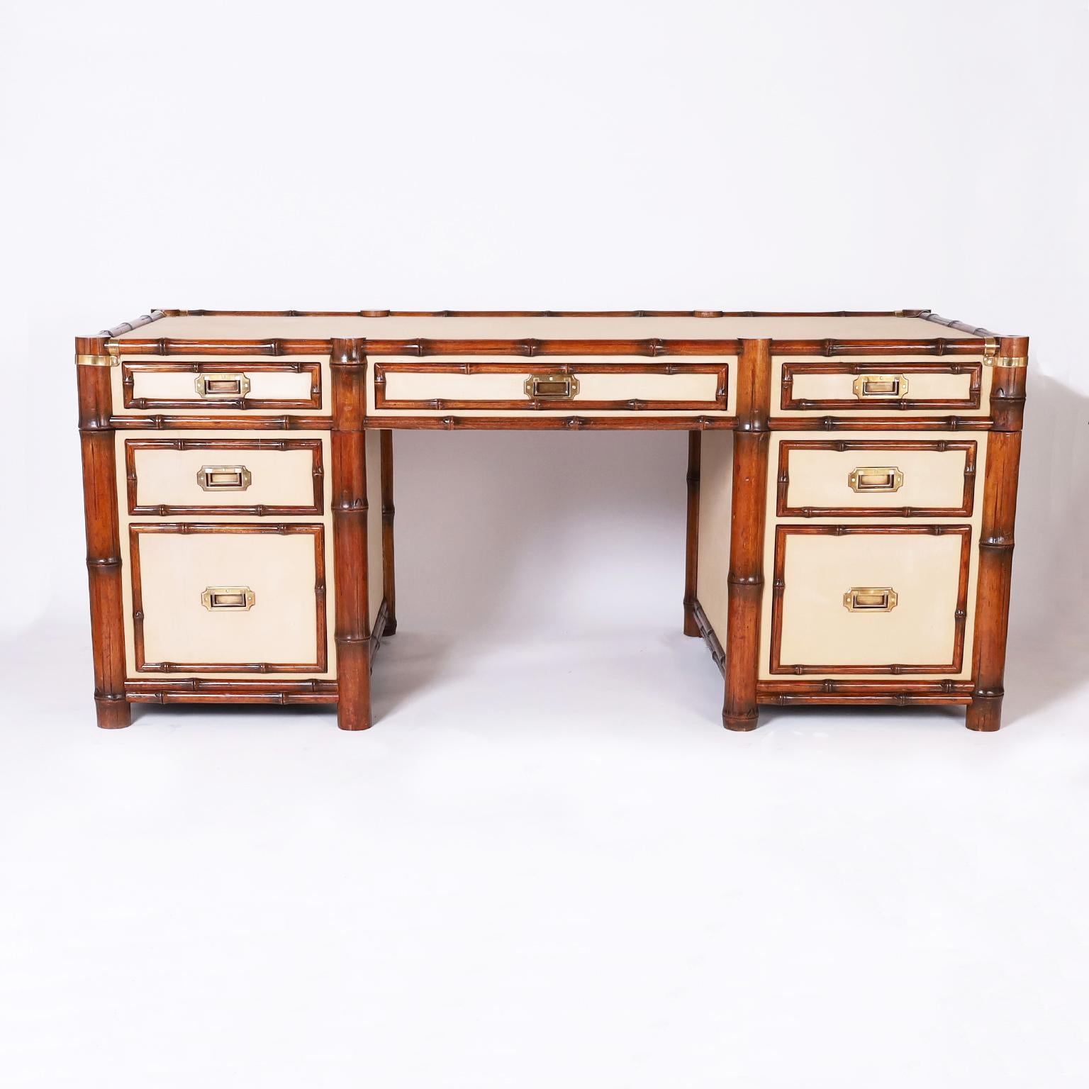 British colonial three piece seven drawer desk with a bamboo frame and panels of tan canvas on the top, sides, front, and back., attributed to Ralph Lauren.The drawer fronts are paneled with bamboo and have brass campaign style hardware. Can be used