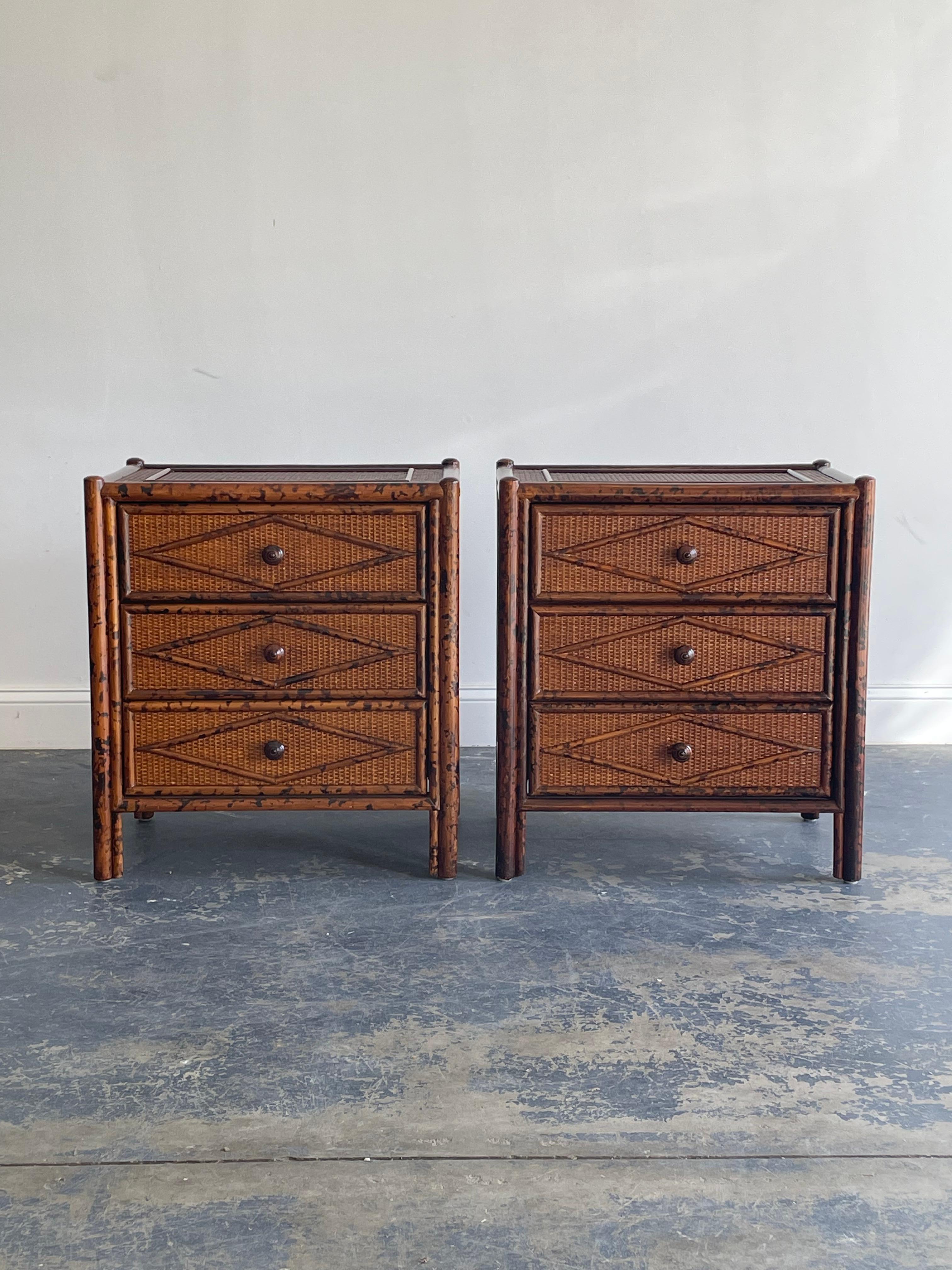 Classic pair of British Colonial nightstands or bedside chests. Features a geometric pattern on drawer fronts, top, and sides. Excellent combination of faux burnt bamboo along with cane. These are often regarded as being English but were made for