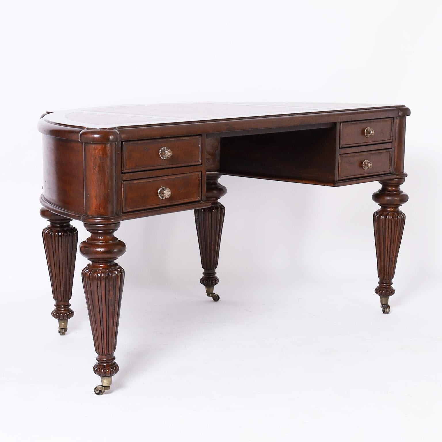 British colonial style desk crafted in mahogany in a demilune form with a tooled tan leather top, four drawers and featuring bold turned and beaded legs on brass casters.