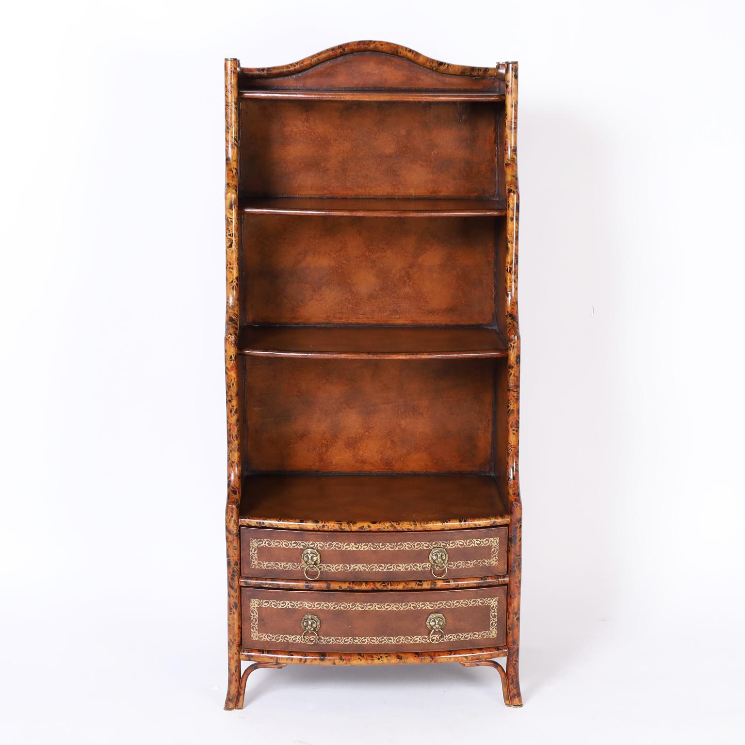 British colonial style bookcase or etagere featuring a faux bamboo frame, tooled leather panels on the sides, shelves, and drawer fronts having classic lion head hardware. Attributed to Maitland-Smith.