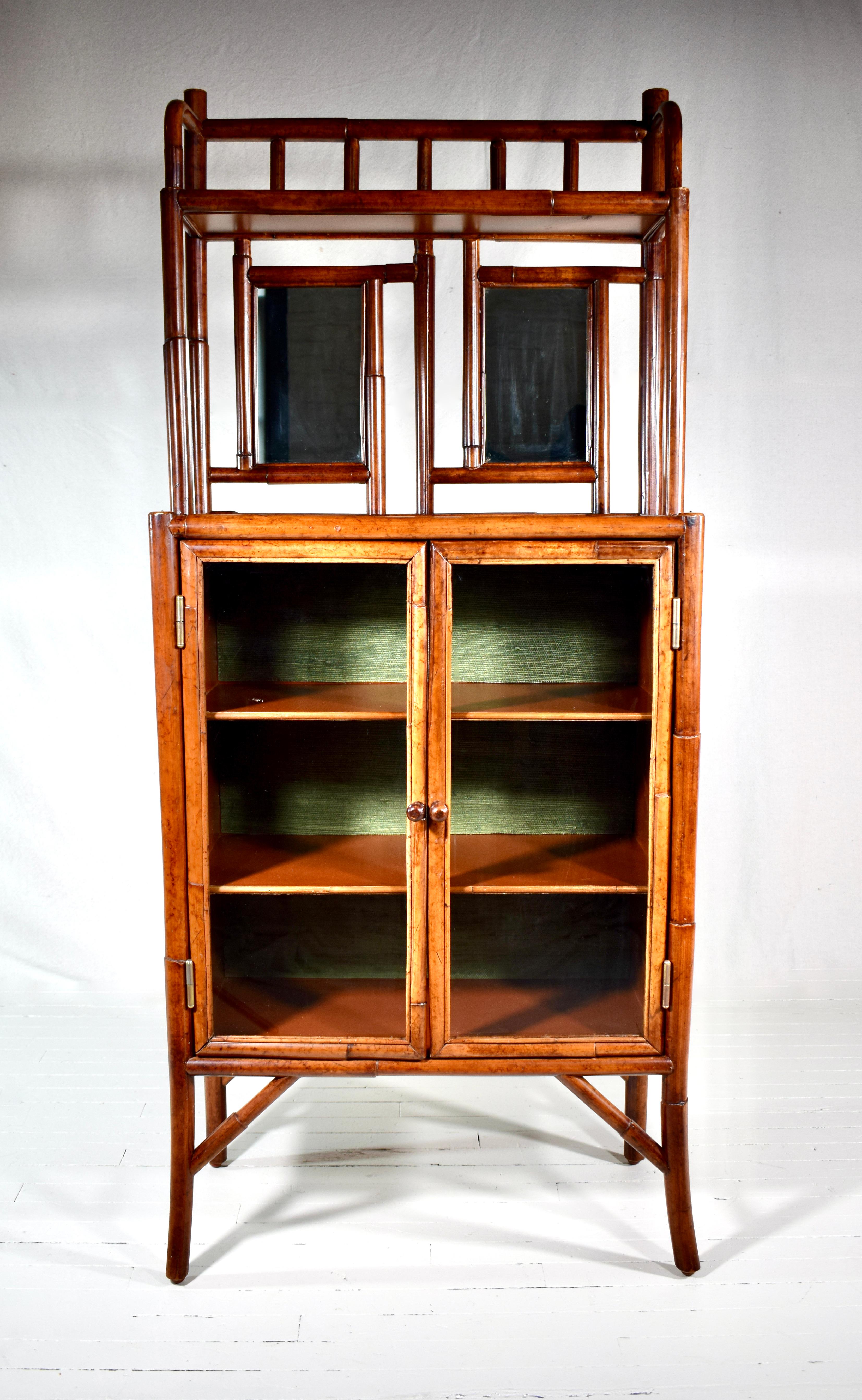 A Faux bamboo British Colonial style etagere with mirror detailing, fixed interior shelves behind two glass doors; enhanced with green grasscloth interior. Multifunctional for storage and display options. Excellent vintage condition; circa 1990's
