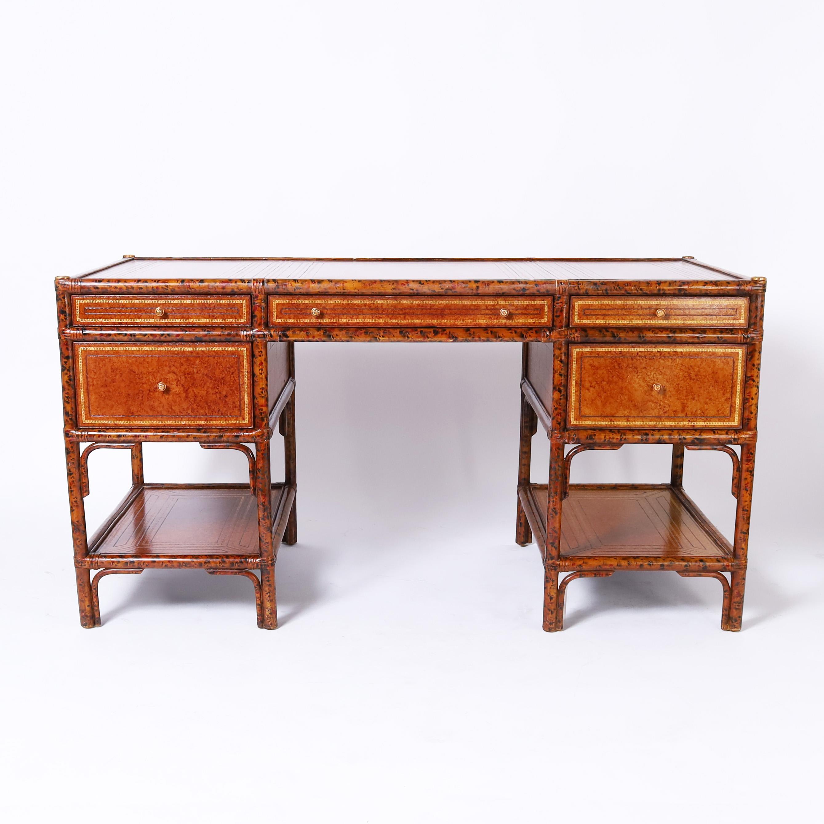 Impressive Mid Century desk crafted with a faux bamboo frame having a faux tortoise finish featuring tooled leather panels on the top, front, side and back, lower tier storage and bent wood brackets. Signed Maitland-Smith in a drawer.