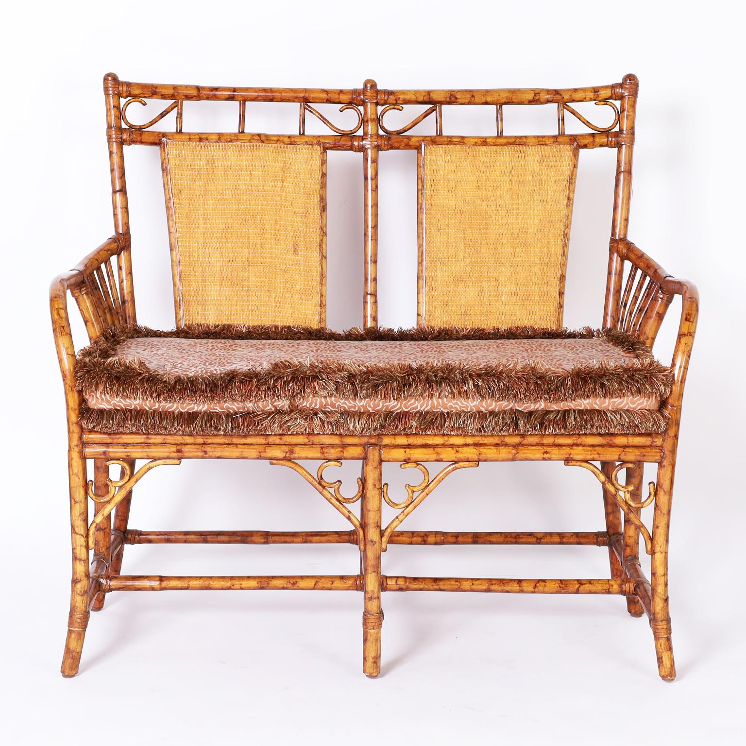 Mid century faux bamboo loveseat or settee featuring two wicker paneled backs, bentwood arms, caned seat under an eccentric cushion, and eight legs with cross stretchers.