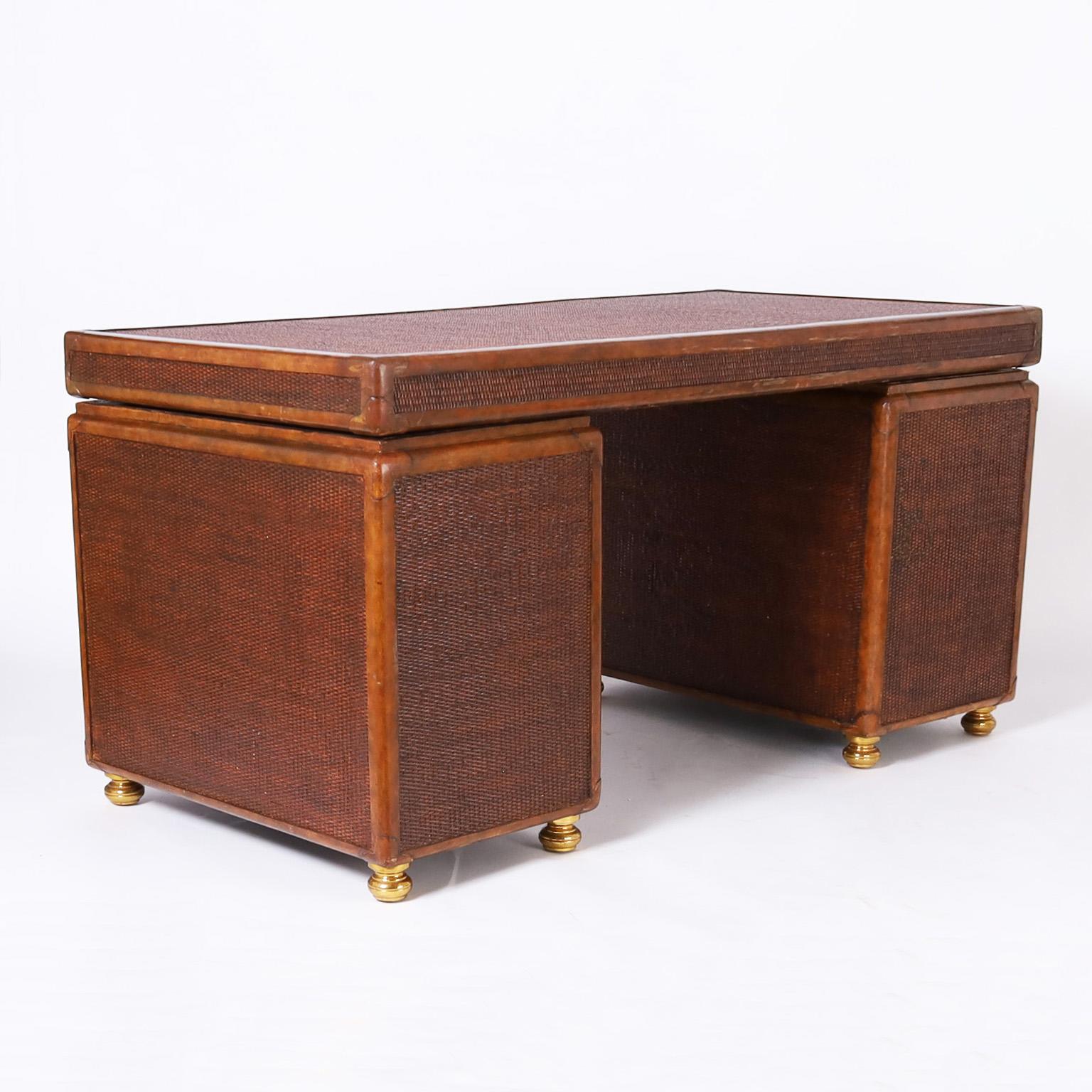 Handsome British colonial style seven drawer desk crafted in mahogany with bold grasscloth panels all around featuring leather luggage style hardware and turned brass legs. Signed Maitland Smith in a drawer.