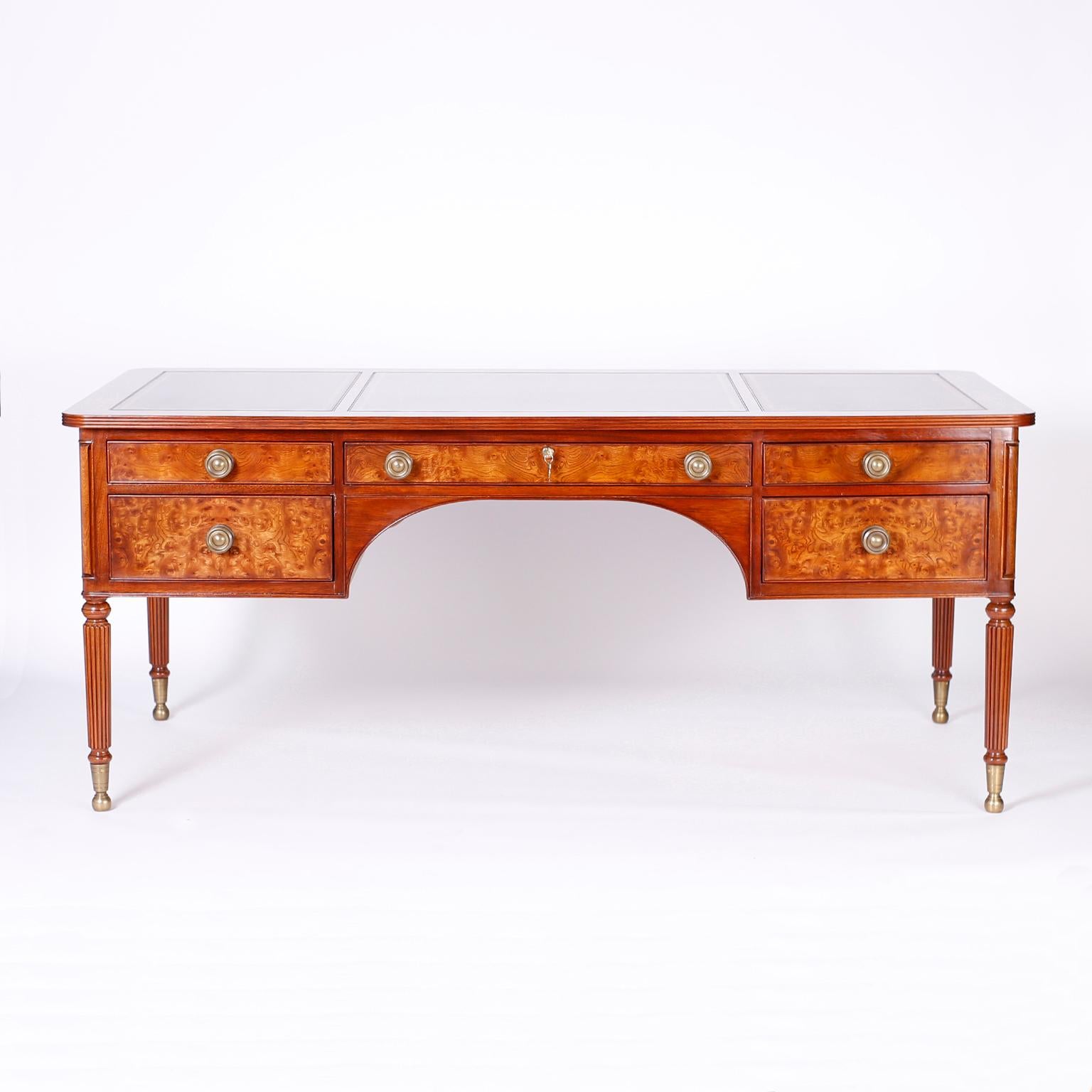 British Colonial Style Leather Top Desk. Five drawer desk crafted in mahogany with a classic form, three tooled brown leather panels on a top with a beaded edge, exotic burled cuts on the drawer fronts and desk sides, brass hardware and turned and