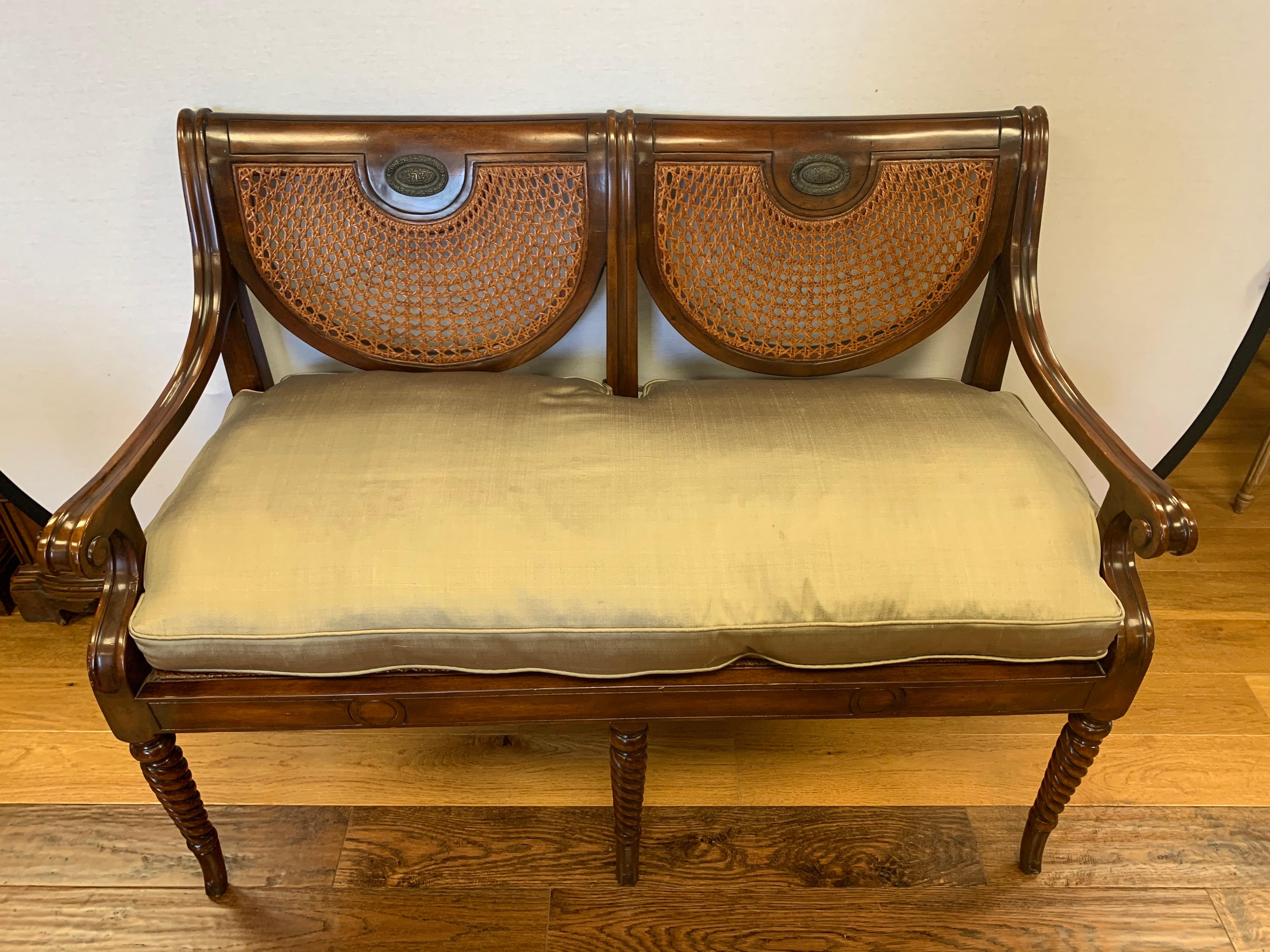 A Regency style mahogany double chair back settee or bench with caned back and seat with scroll arms. Removable down-filled gold silk seat cushion is included. Solid and sturdy throughout.
Measures: 17.75” seat without cushion, 22” with cushion.
