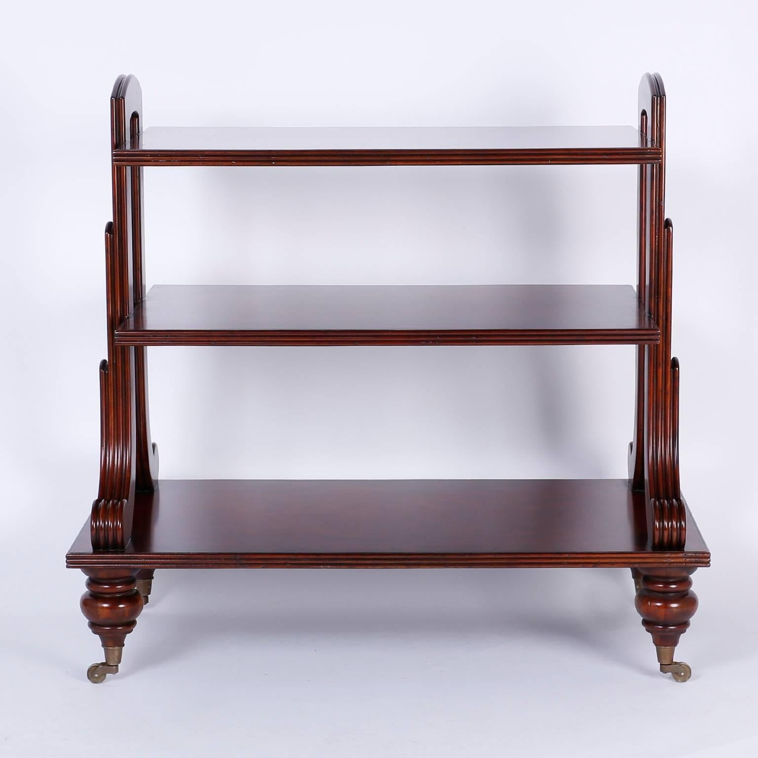 Refined British Colonial style bar with three serving tiers each with dramatic grained mahogany crossbanding and beaded edges. The unusual side supports have paw feet and handles at the top. All this on turned legs with brass casters.