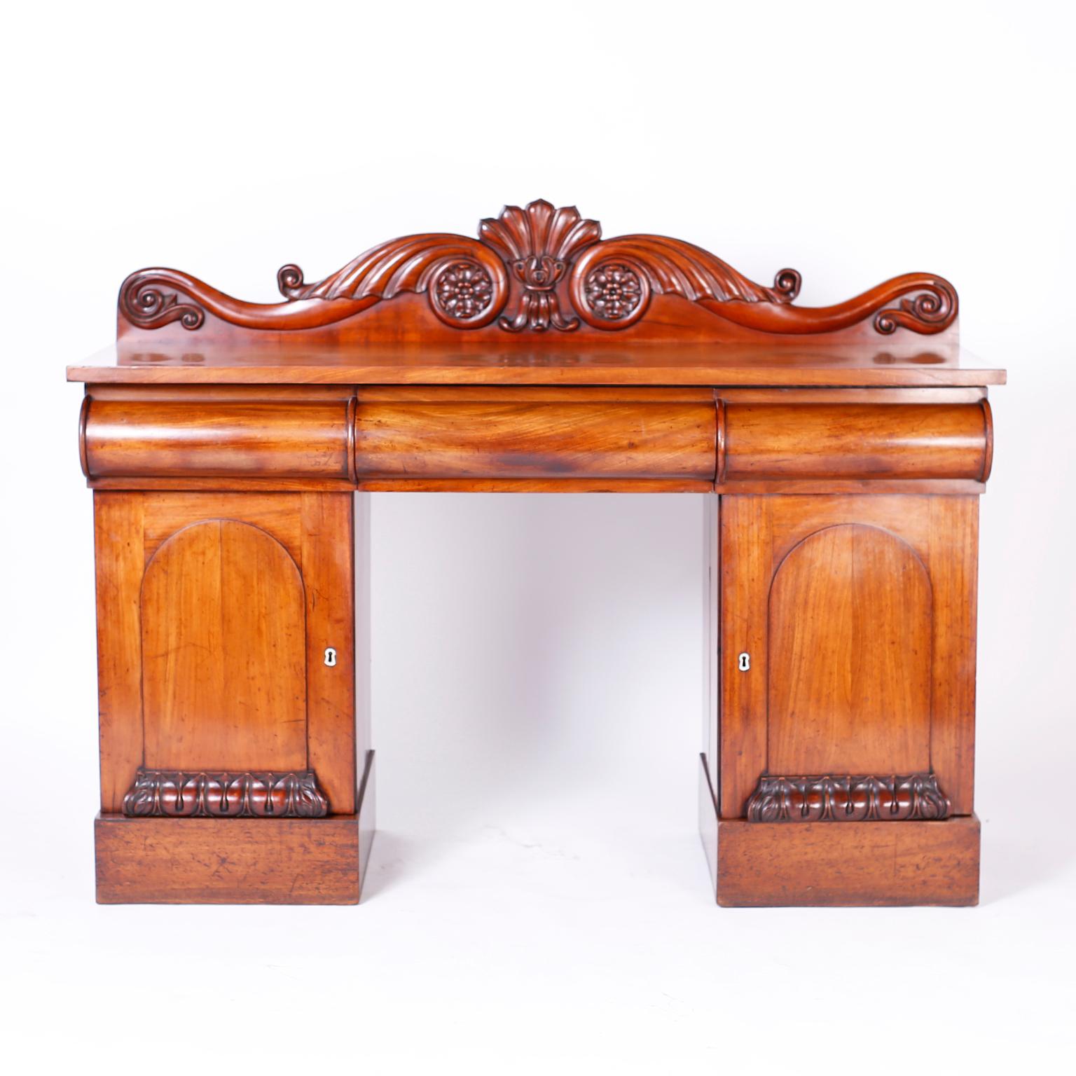 Antique William IV style sideboard reminiscent of a West Indies British Colonial server or buffet crafted in indigenous mahogany with a graceful carved backsplash, well grained top, three convex drawer fronts and cabinet doors with carved acanthus