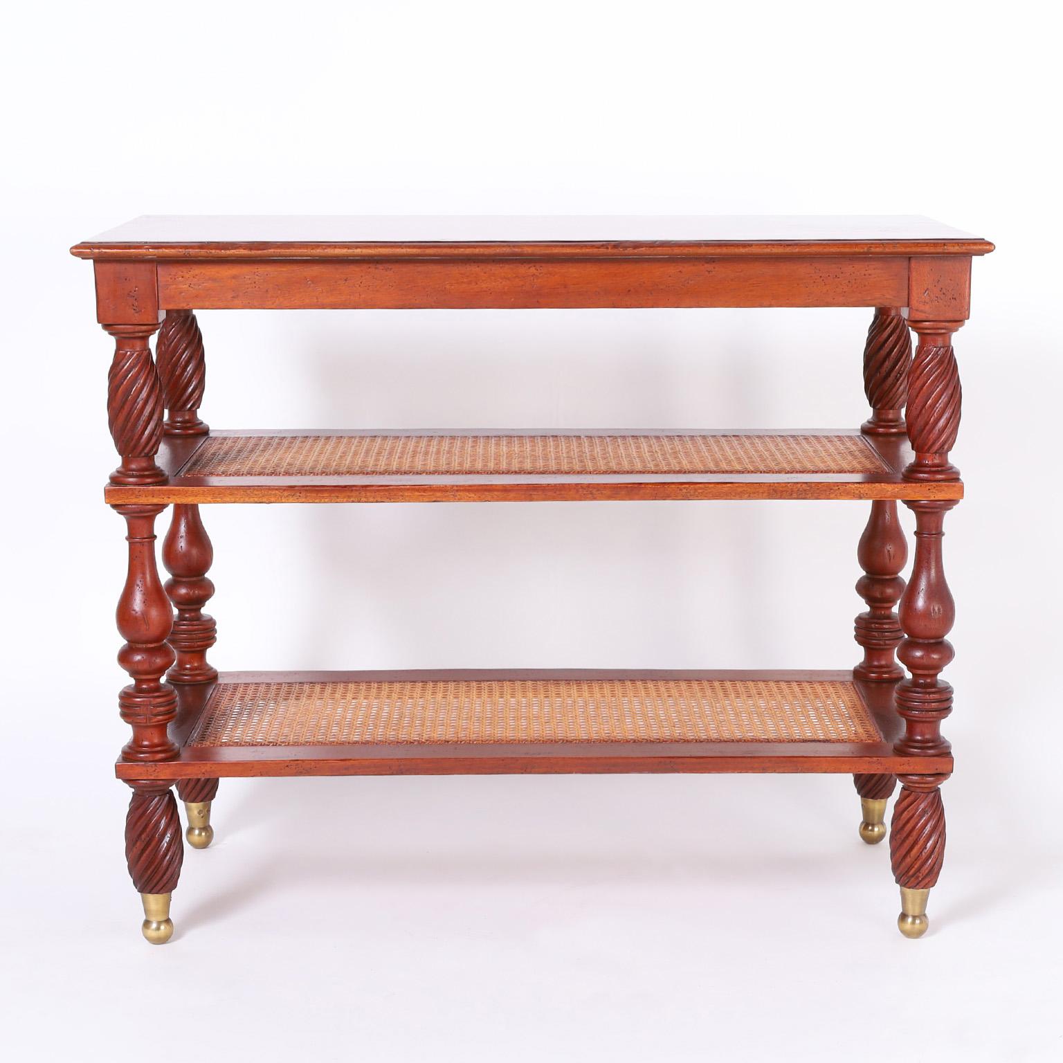 Handsome British Colonial style stand crafted in mahogany with a flame cut top and two lower caned tiers having turned and twisted supports on brass feet. Signed Milling Road Baker on the bottom.