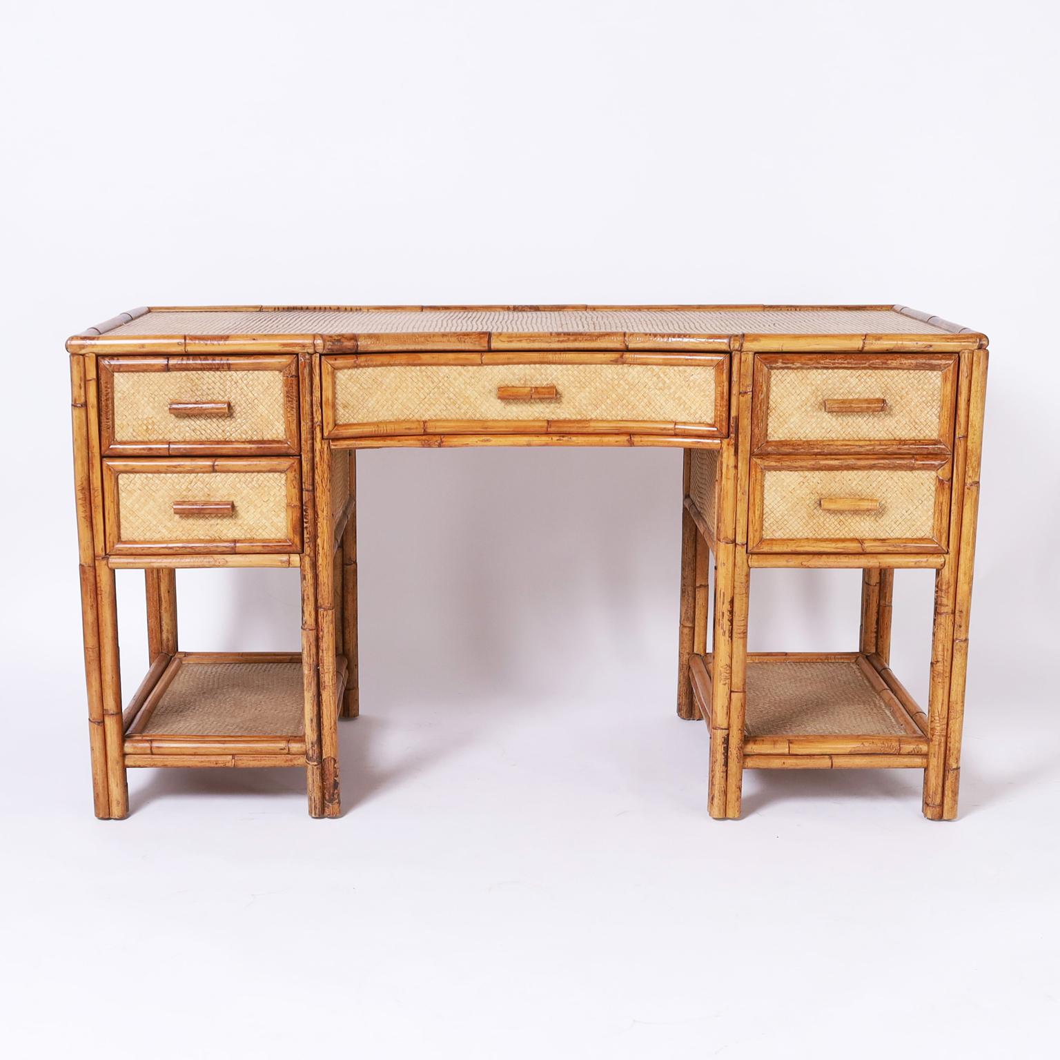 Handsome British Colonial style desk crafted with a bamboo frame and grasscloth panels all around having a concave center drawer and two more on either side over a lower tier. 
