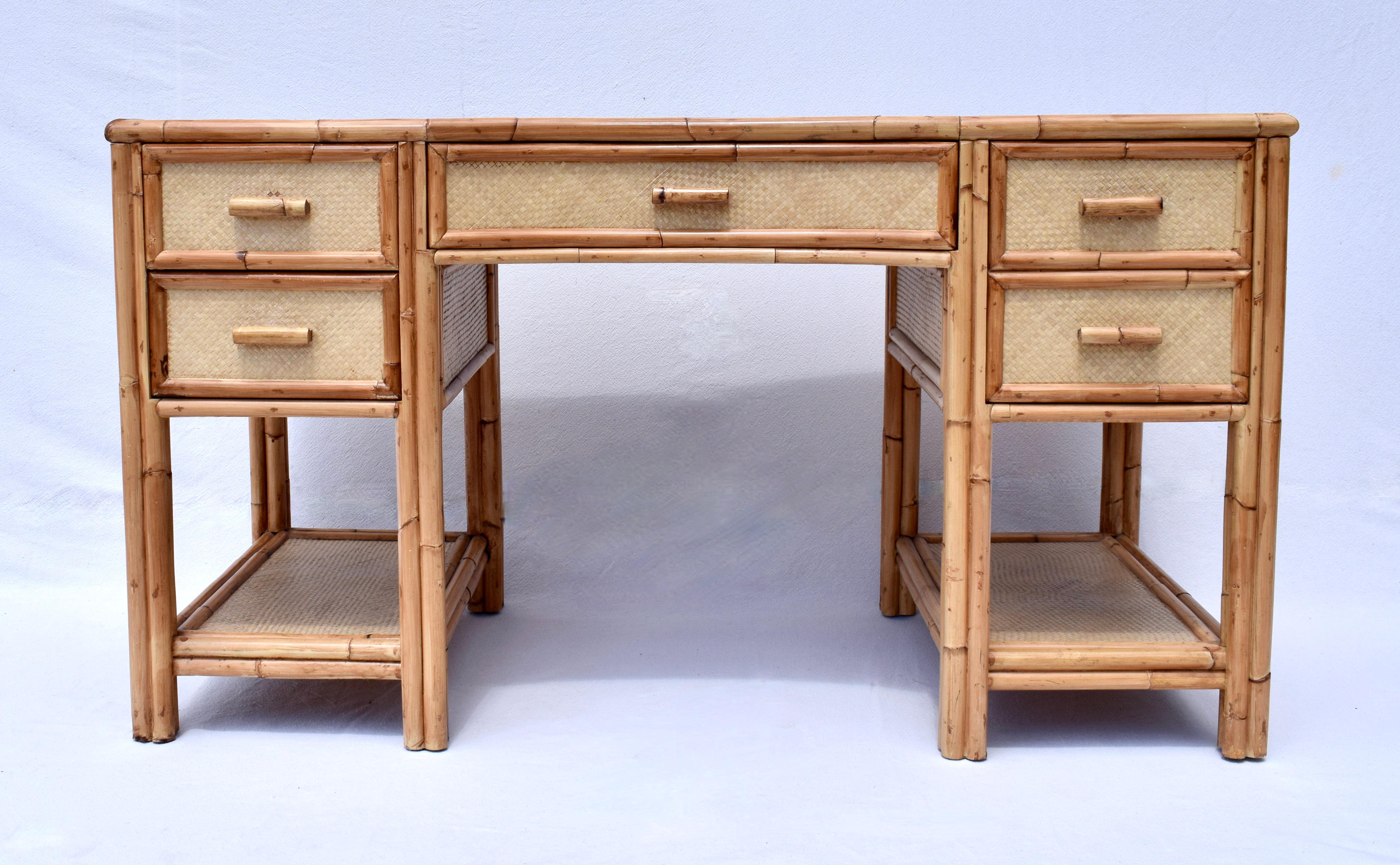 Scrivania o tavolo da lavoro a 4 cassetti in stile British Colonial di metà secolo con struttura in legno di bambù avvolto in rattan intrecciato a canestro. Dotata di una generosa superficie di lavoro con vetro tagliato su misura, montata su ripiani