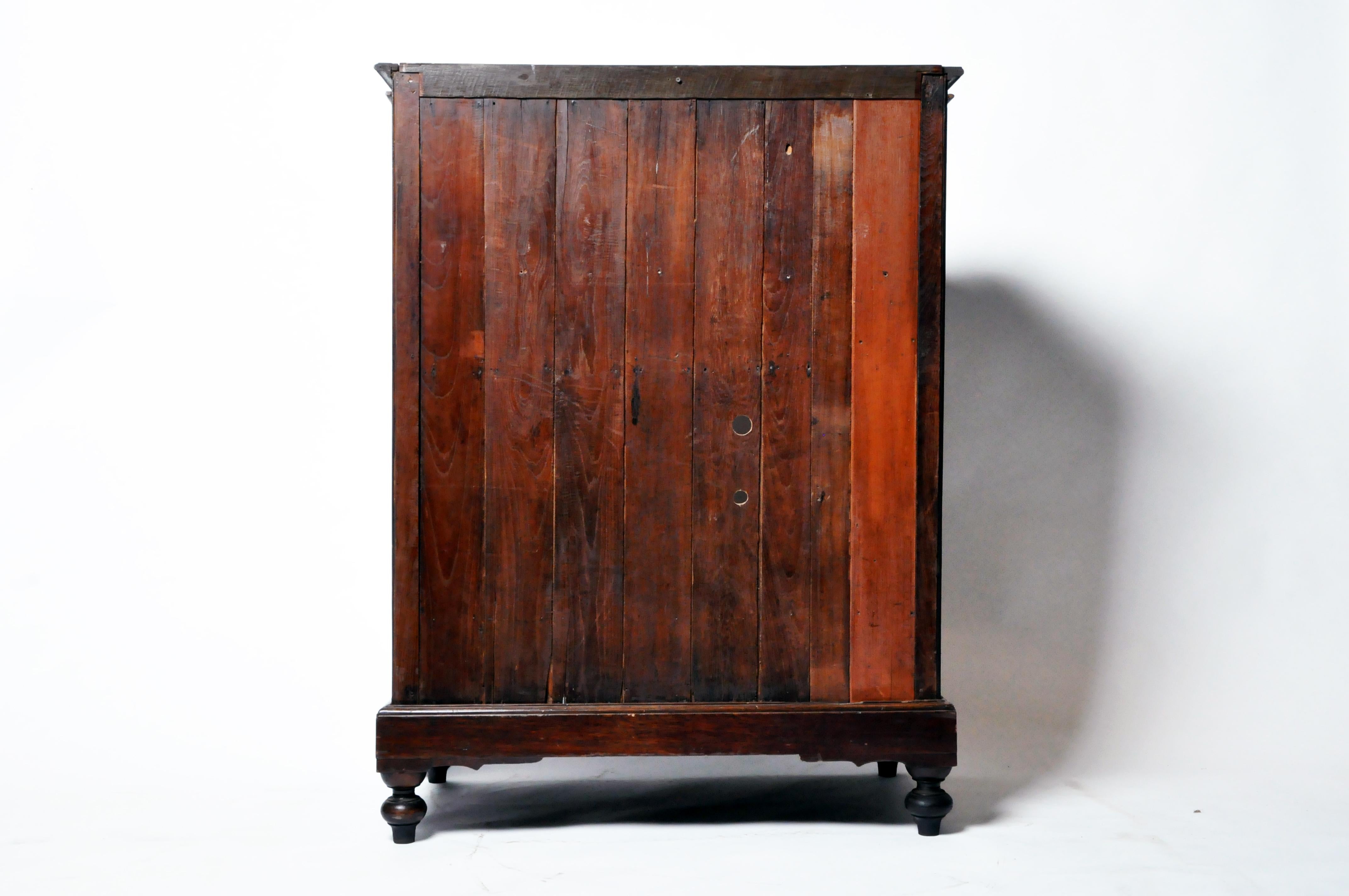 This British Colonial cabinet is from Burma and was made from teak wood in c. 20th century. The handsome piece features a pair of doors and two drawers for storage. The inside of the piece has a shelf for additional storage and more shelves can be