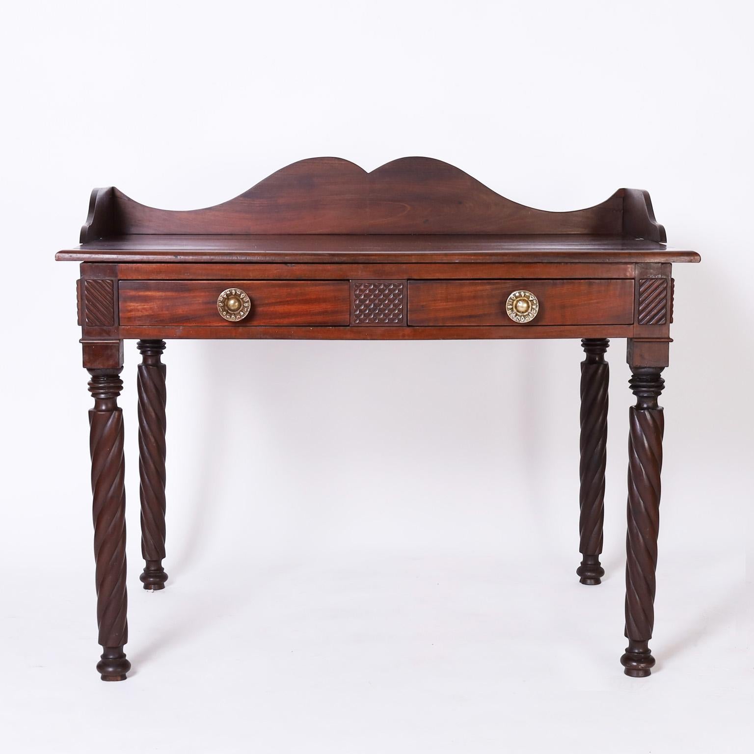 Transporting 19th century British Colonial West Indian writing table or server crafted in mahogany with gallery at the top, two drawers with cast brass hardware, and turned legs.