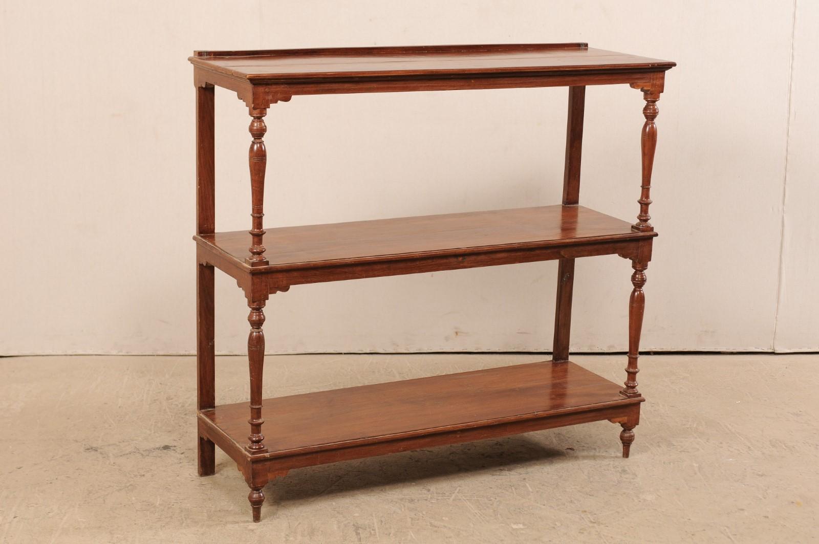 A vintage British Colonial bookshelf with three levels. This freestanding British Colonial shelving unit features three open shelves, supported with nicely turned side columns down front side and straight supports at back. Each shelf apron is
