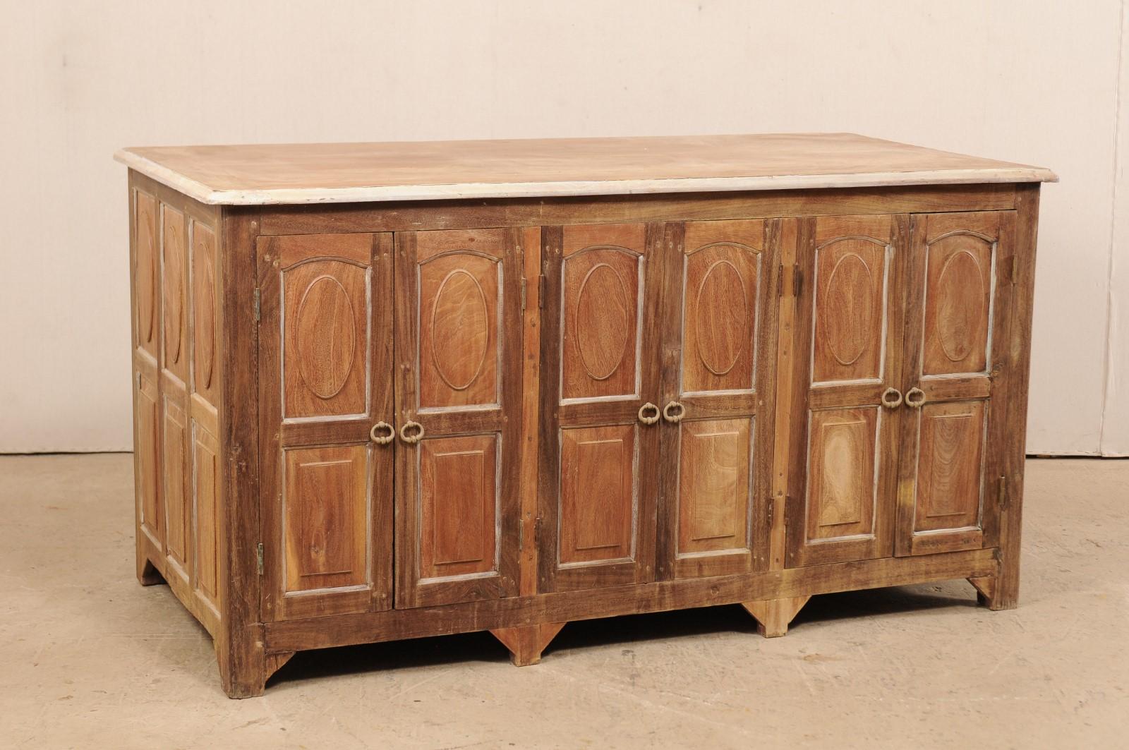 A wonderful British Colonial decoratively paneled work island with abundant storage from the early 20th century. This antique wooden cabinet features a rectangular-shaped top with rounded corners, above a case which is decorated on all sides with