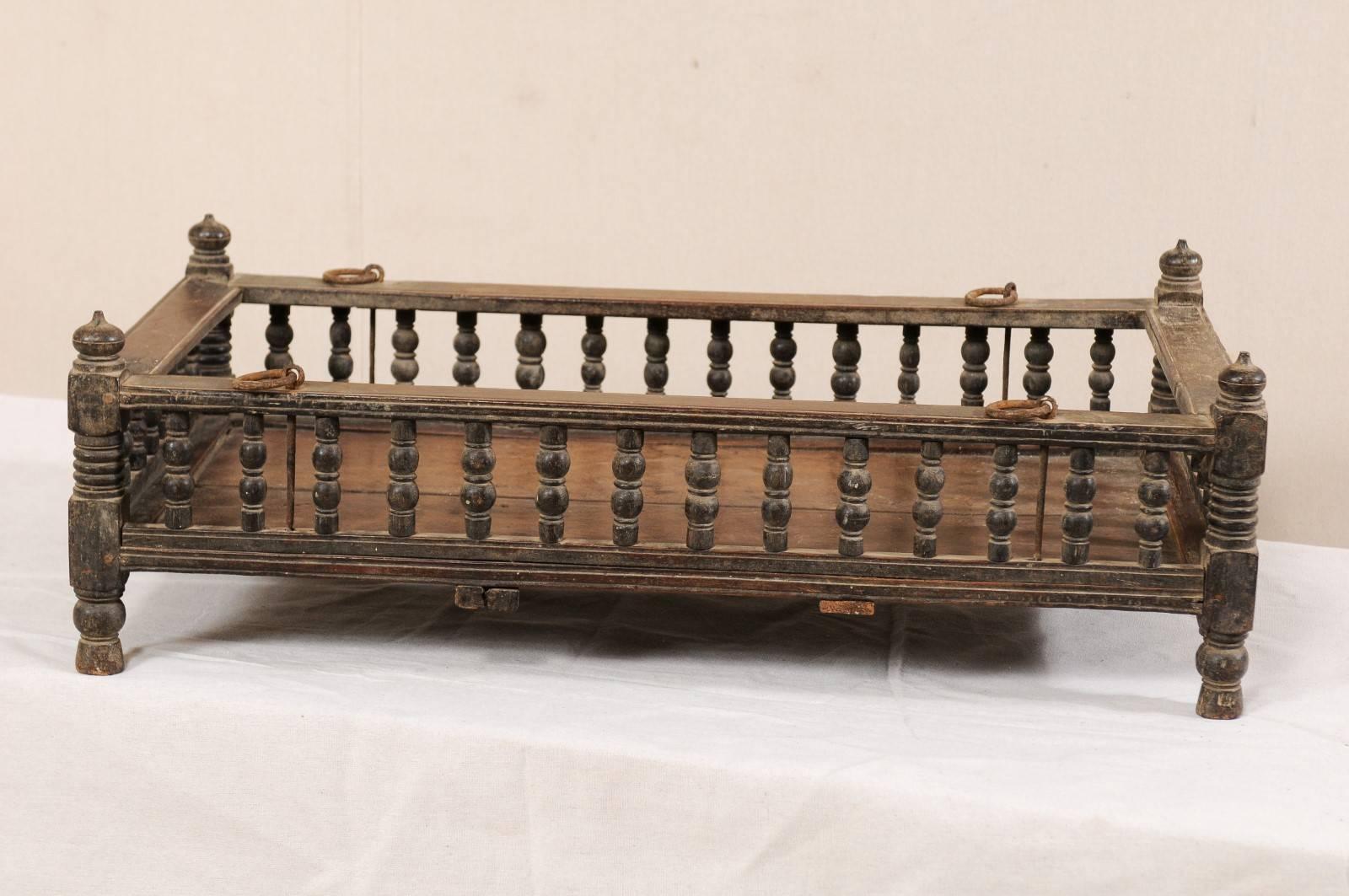 A British Colonial wooden pet bed from the mid-20th century. This vintage Anglo-Indian tropical hardwood piece originated as a baby's bassinet, with petite turned-baluster railing, and finials decorating each corner. The tropical hardwood is a dark