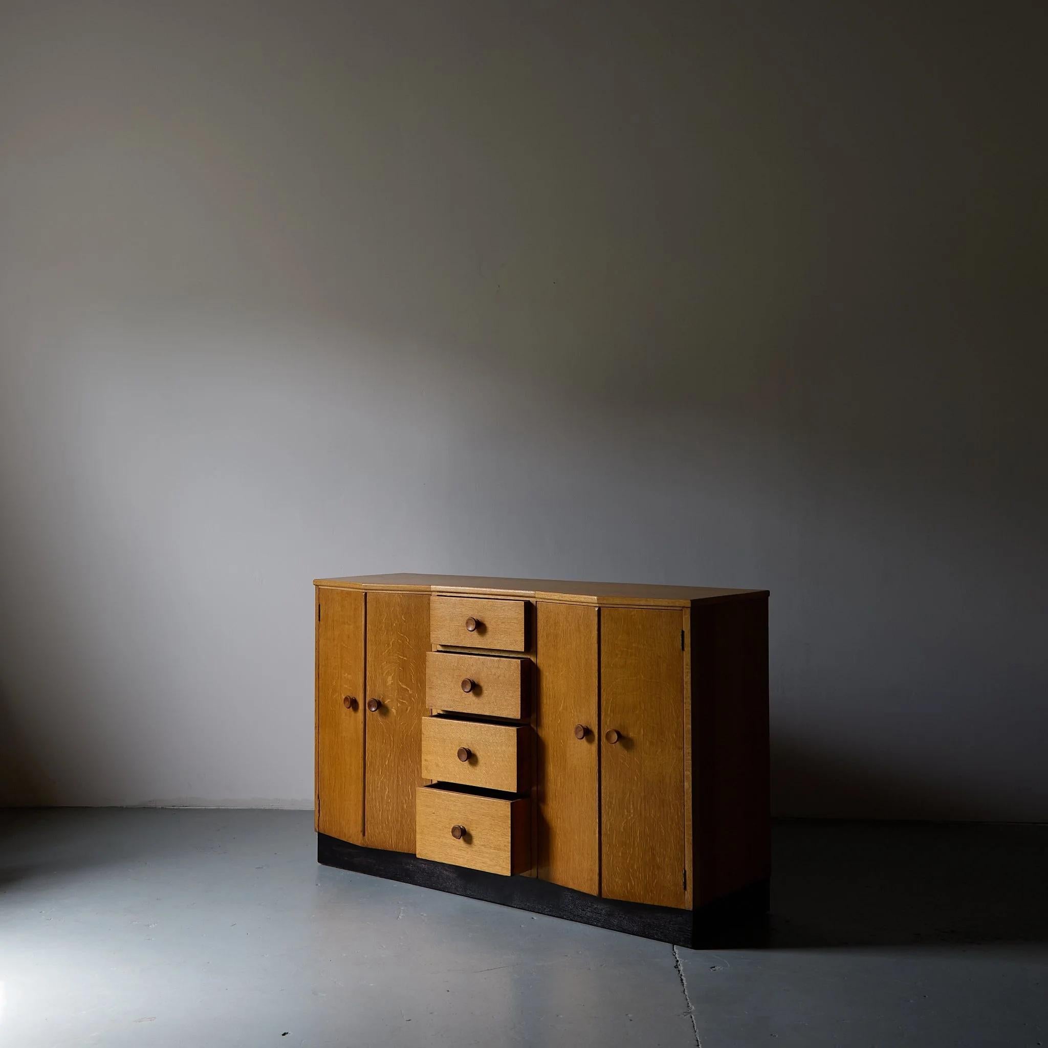 Unusual art deco oak sideboard with faceted cabinet doors on either side of x 4 central drawers. 

Made in the UK by cabinet makers C.W Burnes, the model also appears in the V&A permanent collection. 

British 1950s.

W 138.5cm x H 90cm x D 50 cm