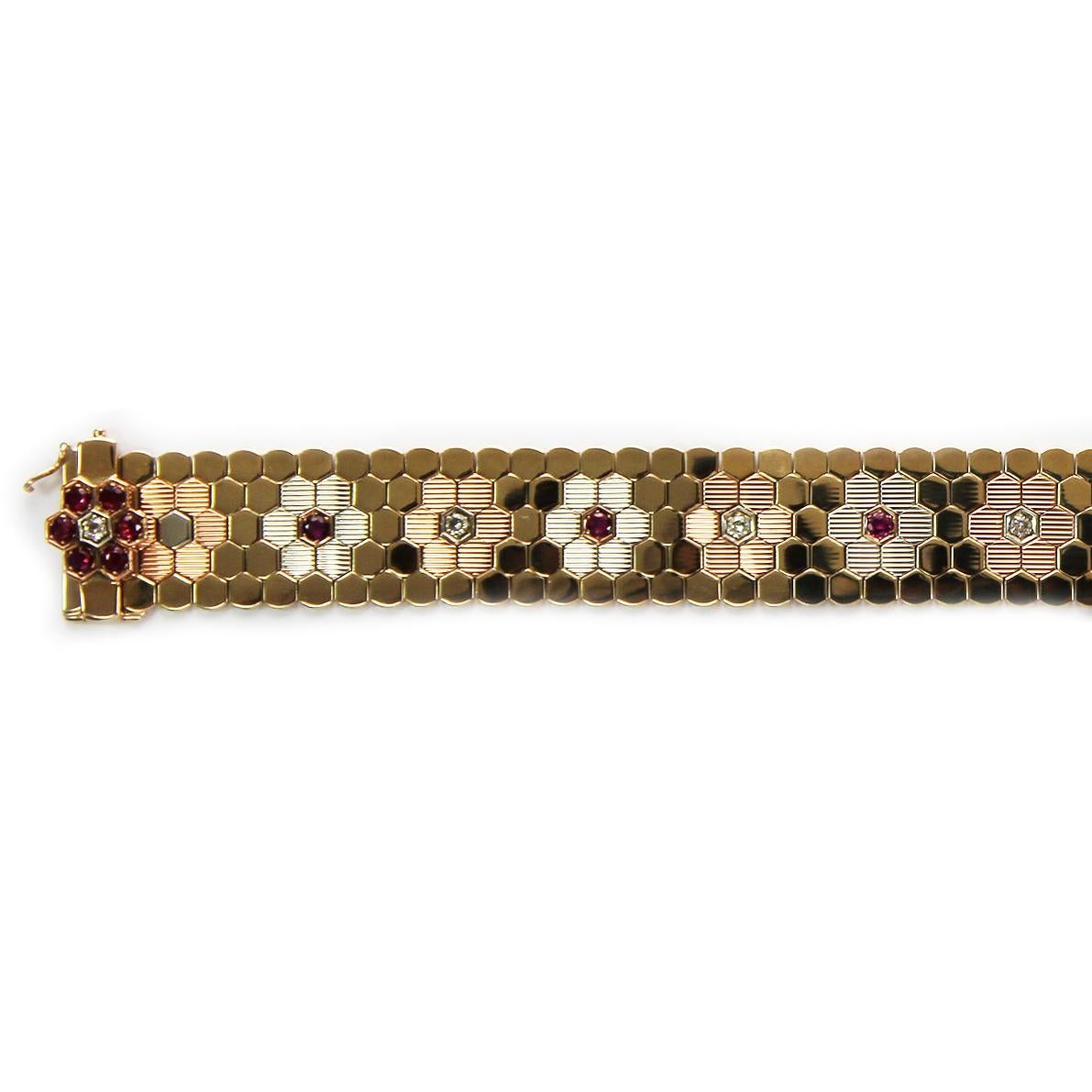 A ruby and diamond honeycomb-style flexible bracelet. The interlocking 9 carat yellow, white and rose gold pieces are arranged into a band patterned with flowers, each with central ruby and diamond points. The bracelet has a double locking safety