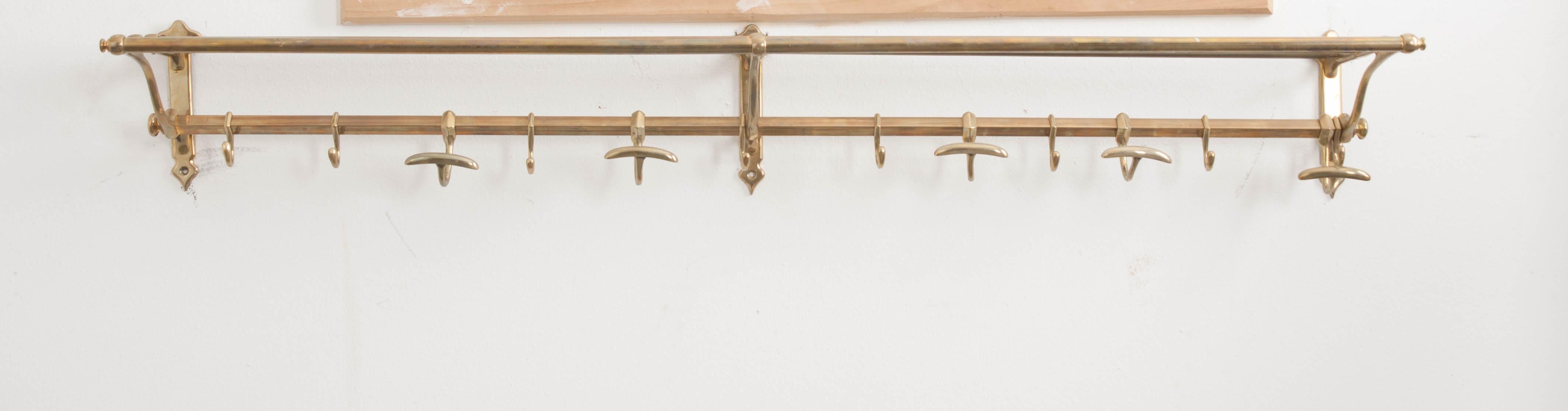 This fine patinated brass train car luggage rack with hat and coat hooks was made in England, circa 1890s, and features an open, tubular shelf supported by three solid brass wall-mounted brackets with another rack below which is outfitted with solid