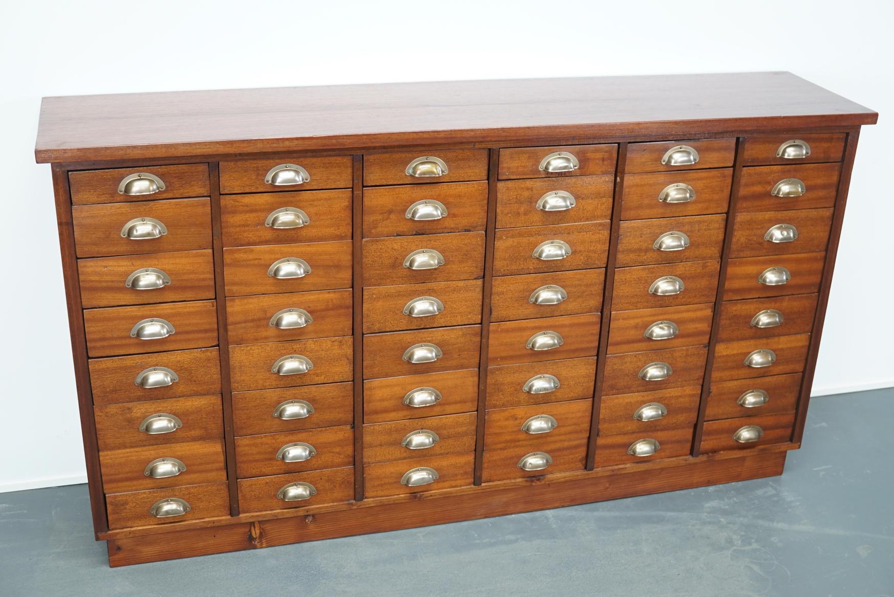 This vintage mahogany bank of drawers dates from the 1930s and was made in England. It features a solid wooden frame and drawers in mahogany with metal cup handles.
  