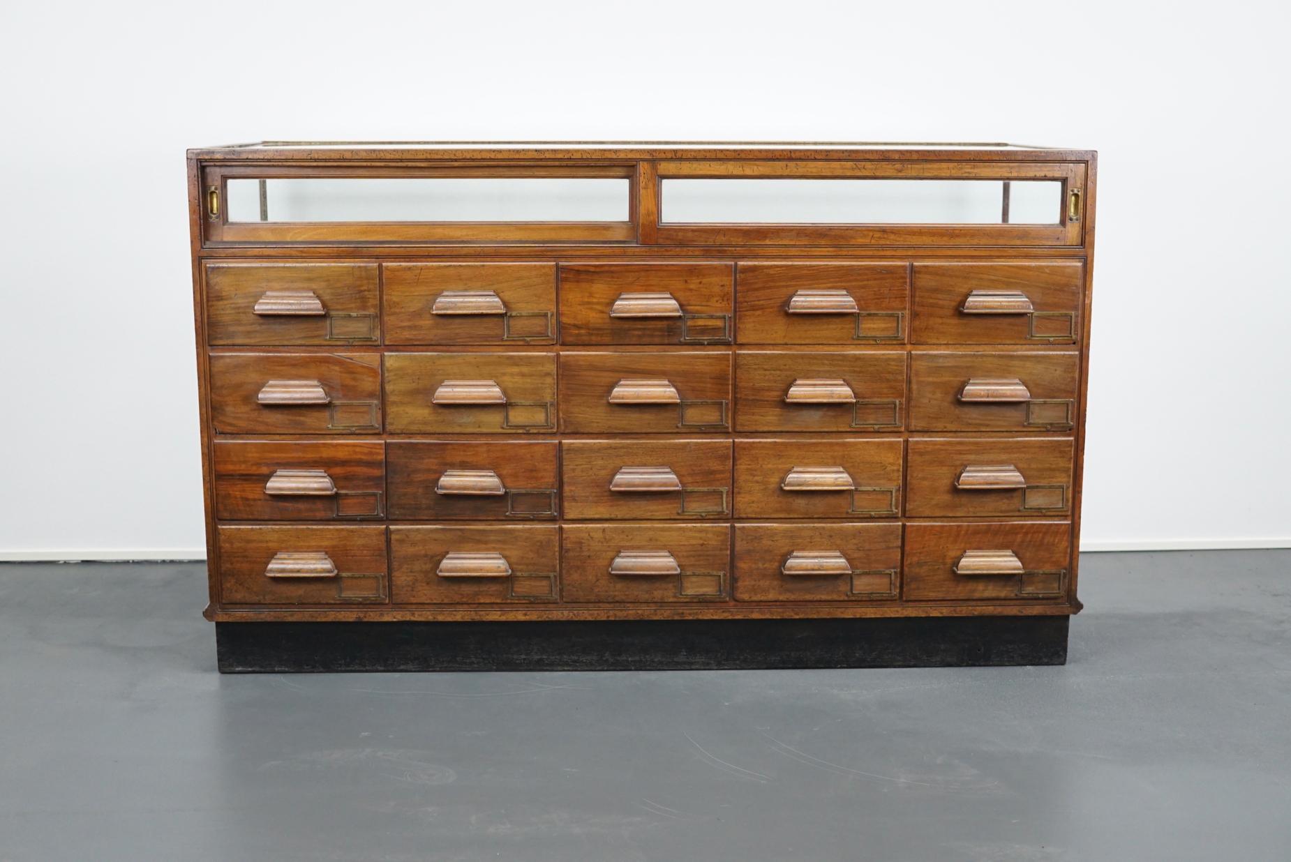 This vintage mahogany haberdashery shop counter dates from the 1930s and was made in England. It features a solid wooden frame and drawers in mahogany with wooden handles.
 