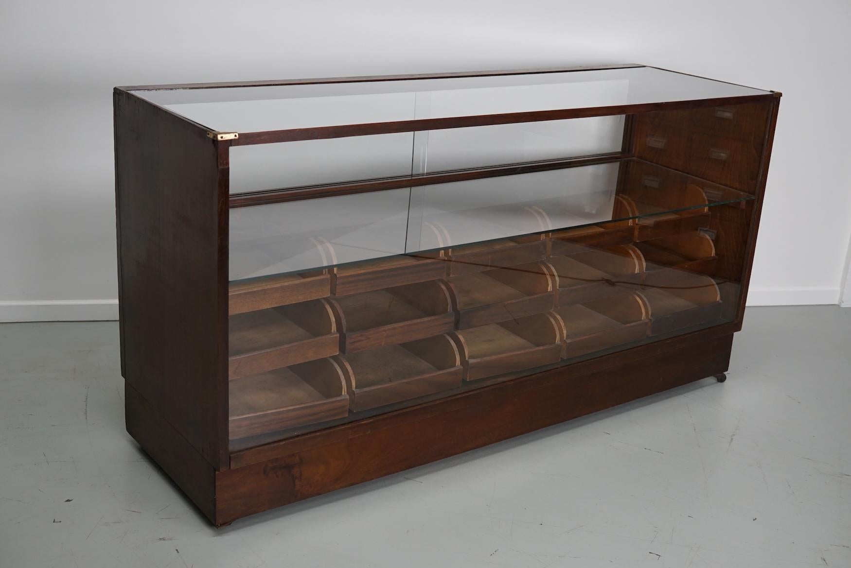 This vintage mahogany haberdashery shop counter dates from the 1940s and was made in England. It features a solid frame with veneered sides, glass casing and drawers in mahogany with copper handles. The drawers measure +- DWH 38 / 43 / 48 x 31 x 40