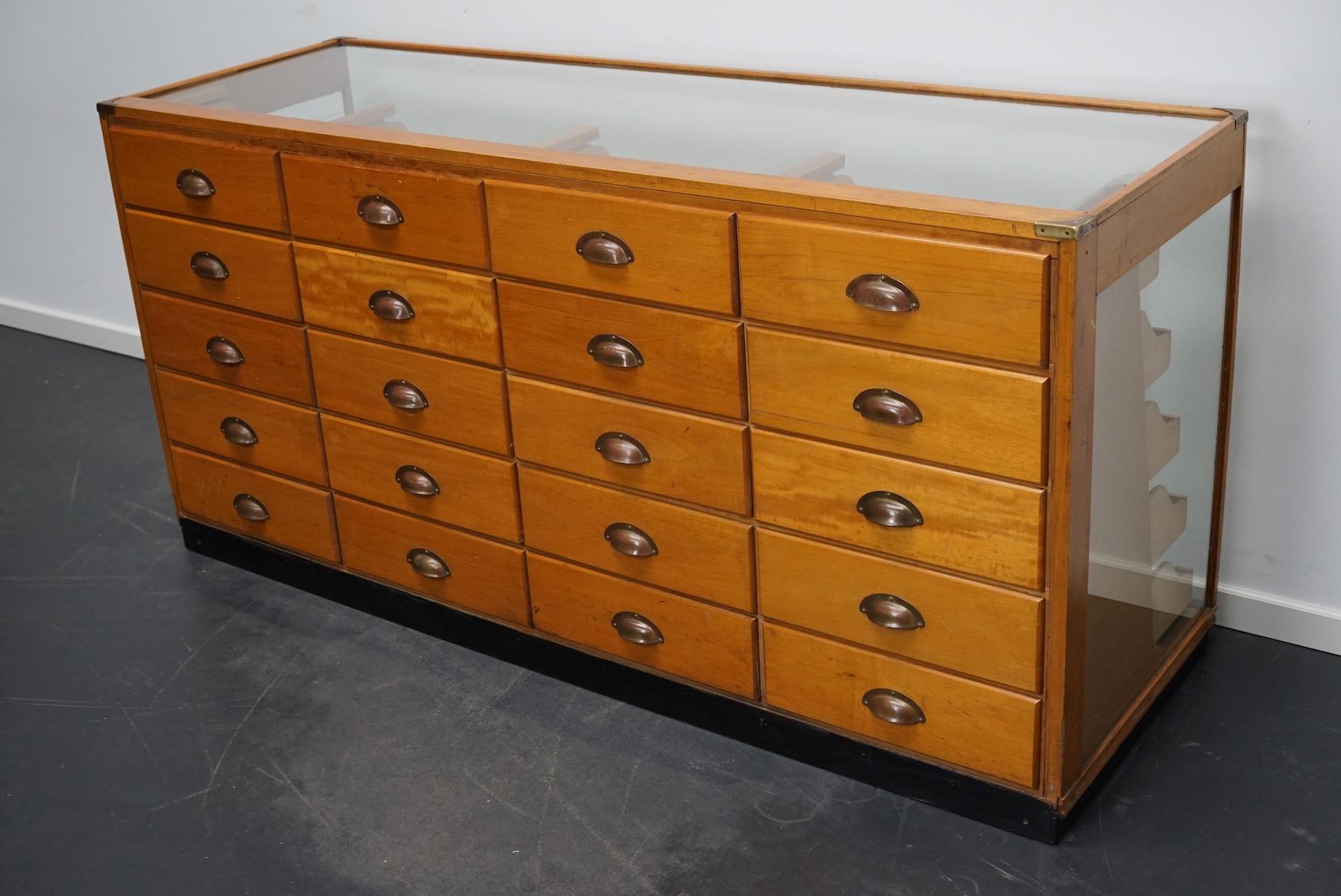 This vintage maple haberdashery shop counter dates from the 1930s and was made in England. It features a solid wooden frame with brass details, a glass casing and drawers in maple with copper handles.
 