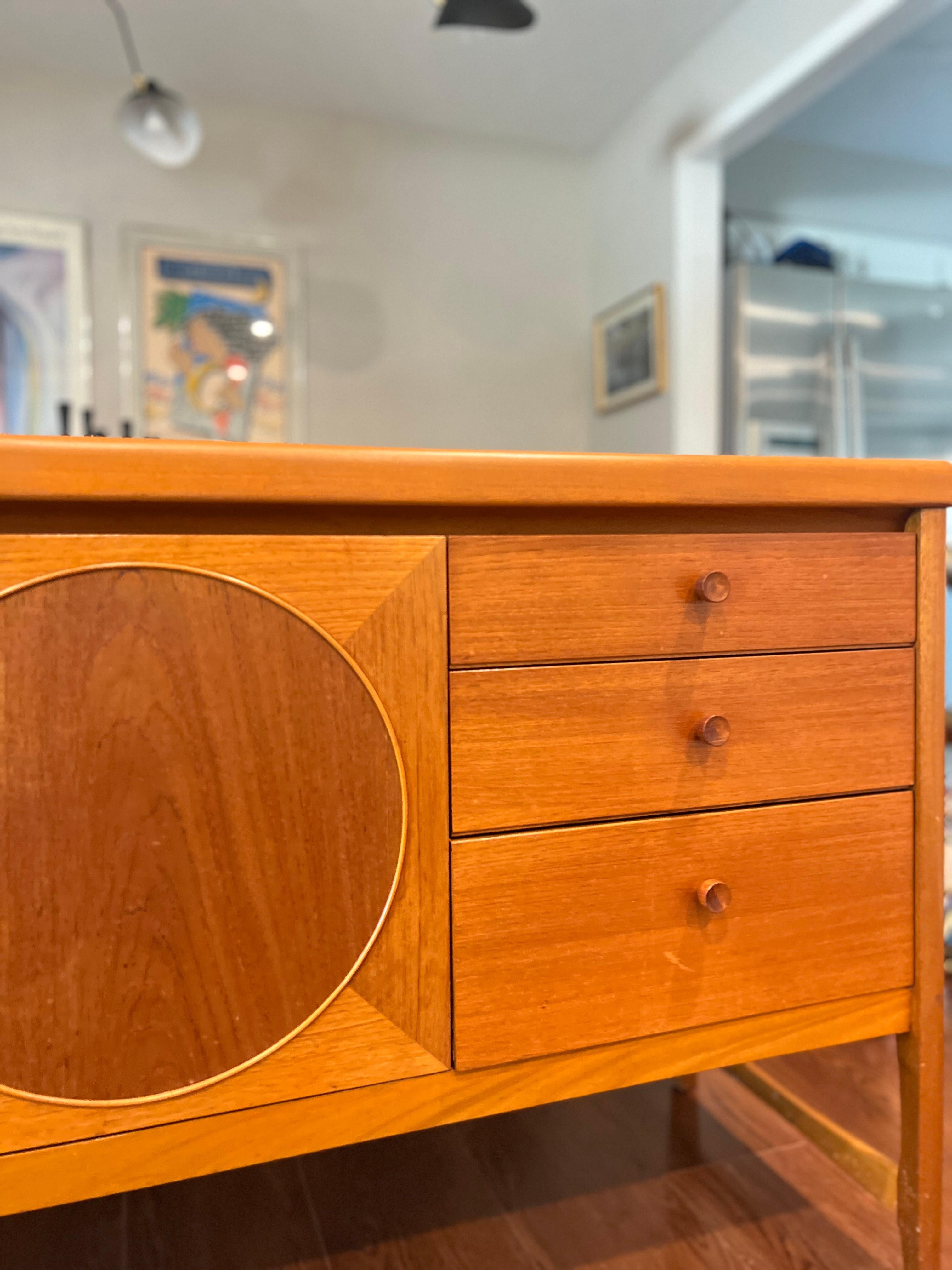 Here is a beautiful British mid century modern teak sideboard by Nathan furniture circa 1960's. This sought after sideboard features a vibrant wood grain, beautiful inlay circle design details on its three front doors, a bank of three drawers and a