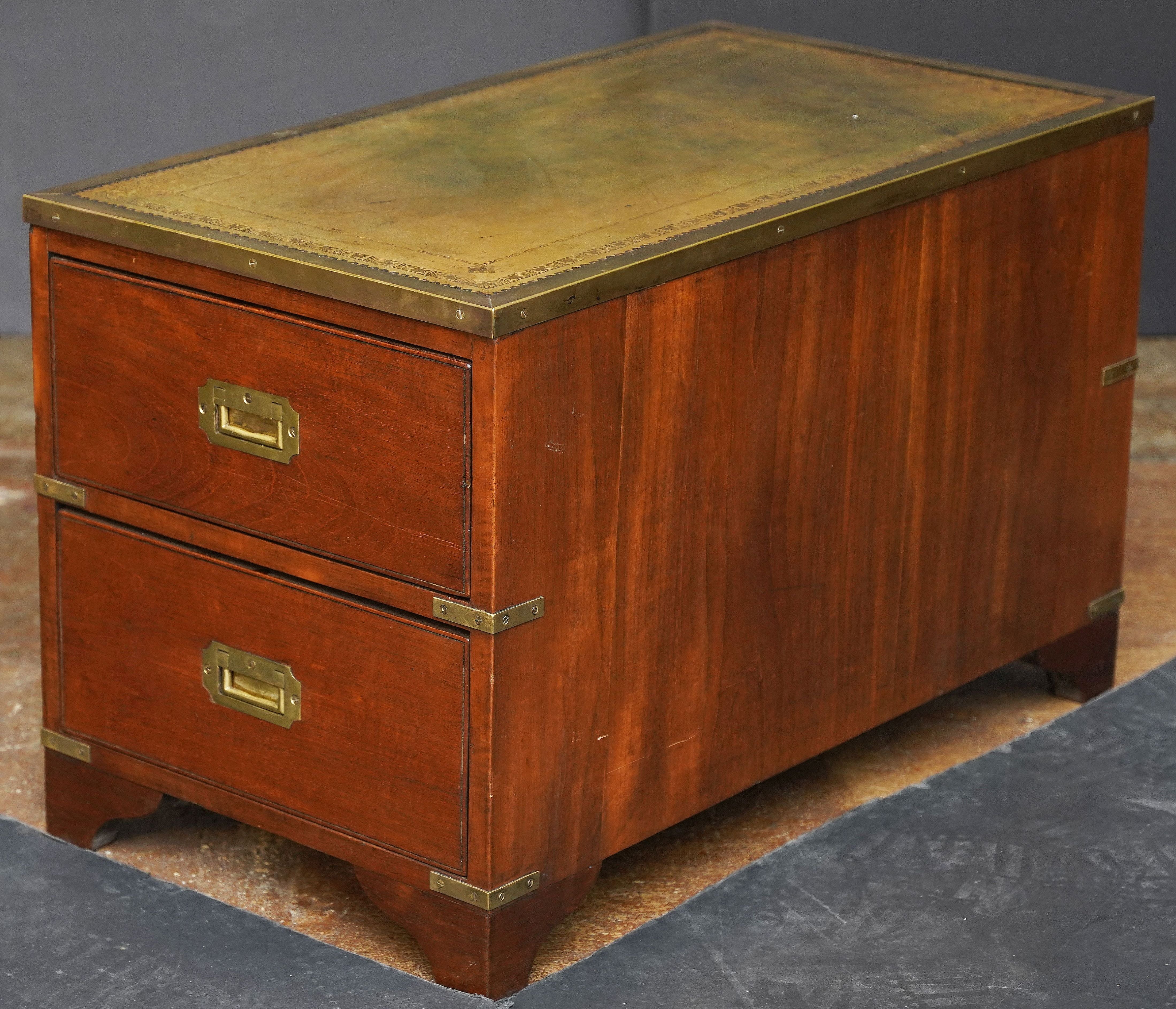 A handsome British military officer’s Campaign Ware cabinet or low table from the early 20th century, featuring a rectangular brass-bound patinated teak exterior, with embossed leather top, enclosing two drawers fitted with brass escutcheons and