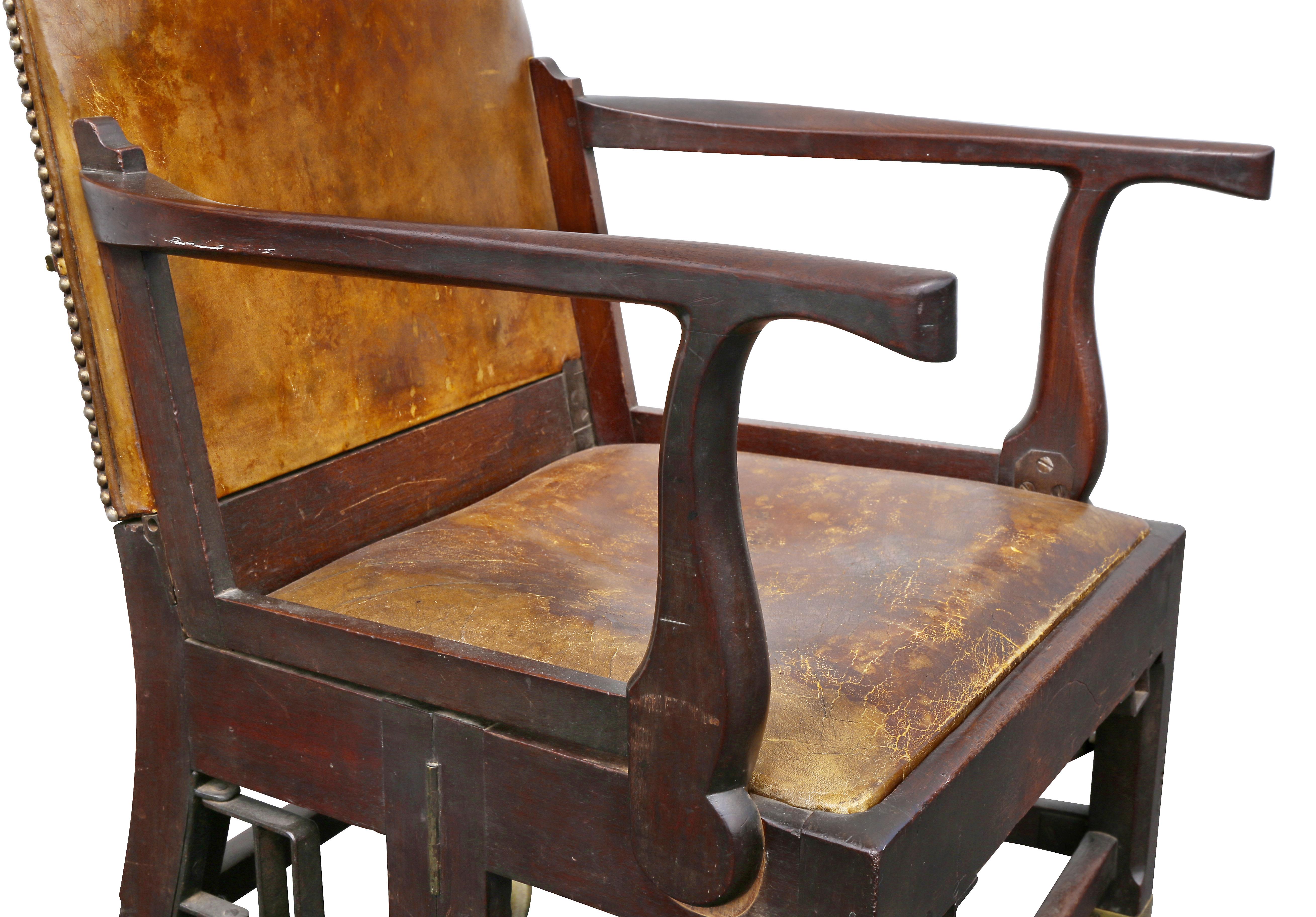 Avec un dossier serpentin tapissé de cuir brun, des accoudoirs et un siège en cuir, le tout reposant sur des pieds à section carrée reliés par un châssis en caisson reposant sur de grandes roulettes en laiton. La chaise se replie pour être