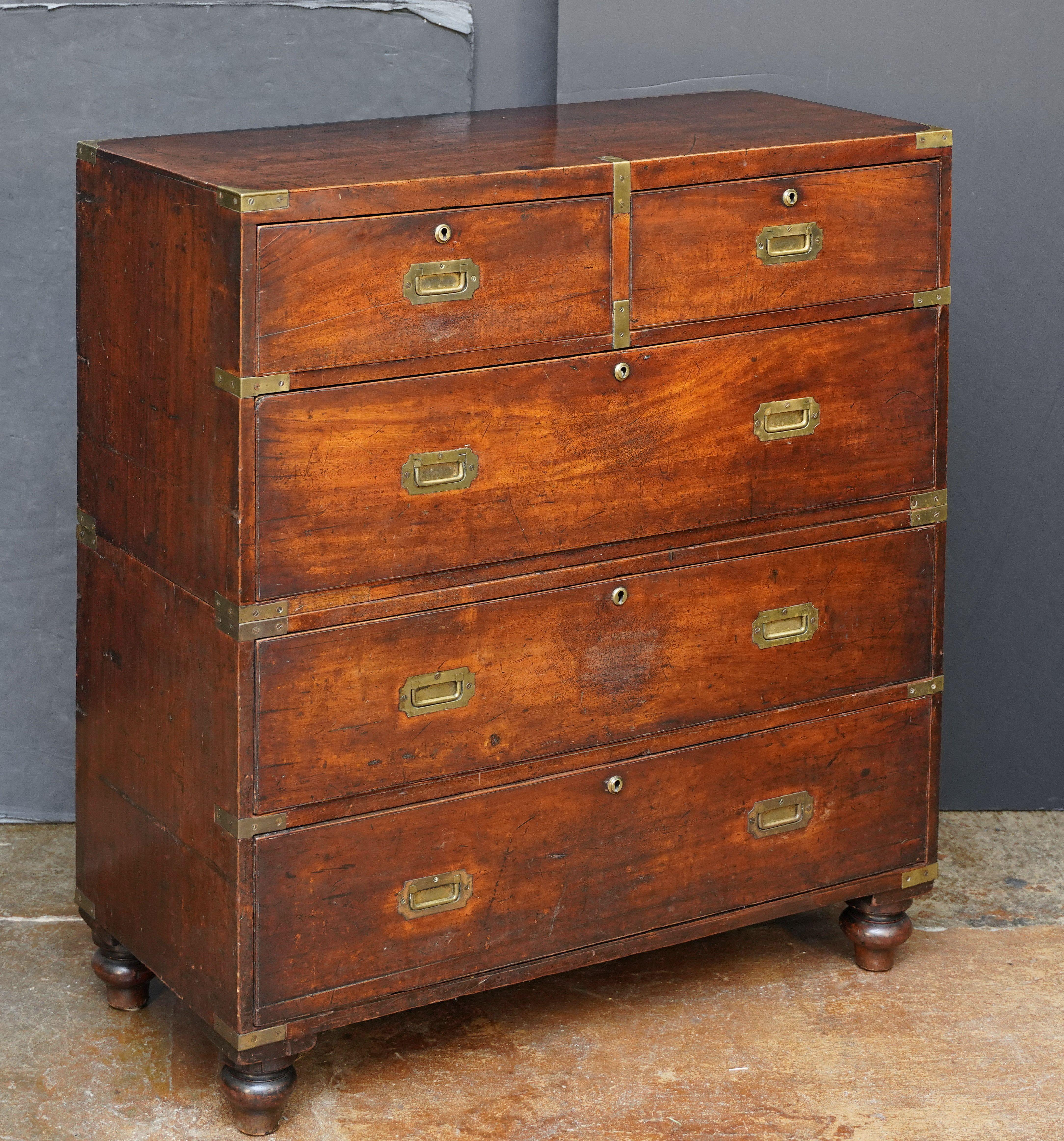 Bonita cómoda o cajonera de campaña de oficial militar británico del siglo XIX, con exterior de caoba patinada sobre cinco cajones con escudos de latón y tiradores embutidos. El arcón, encuadernado en latón, consta de dos partes -la mitad superior
