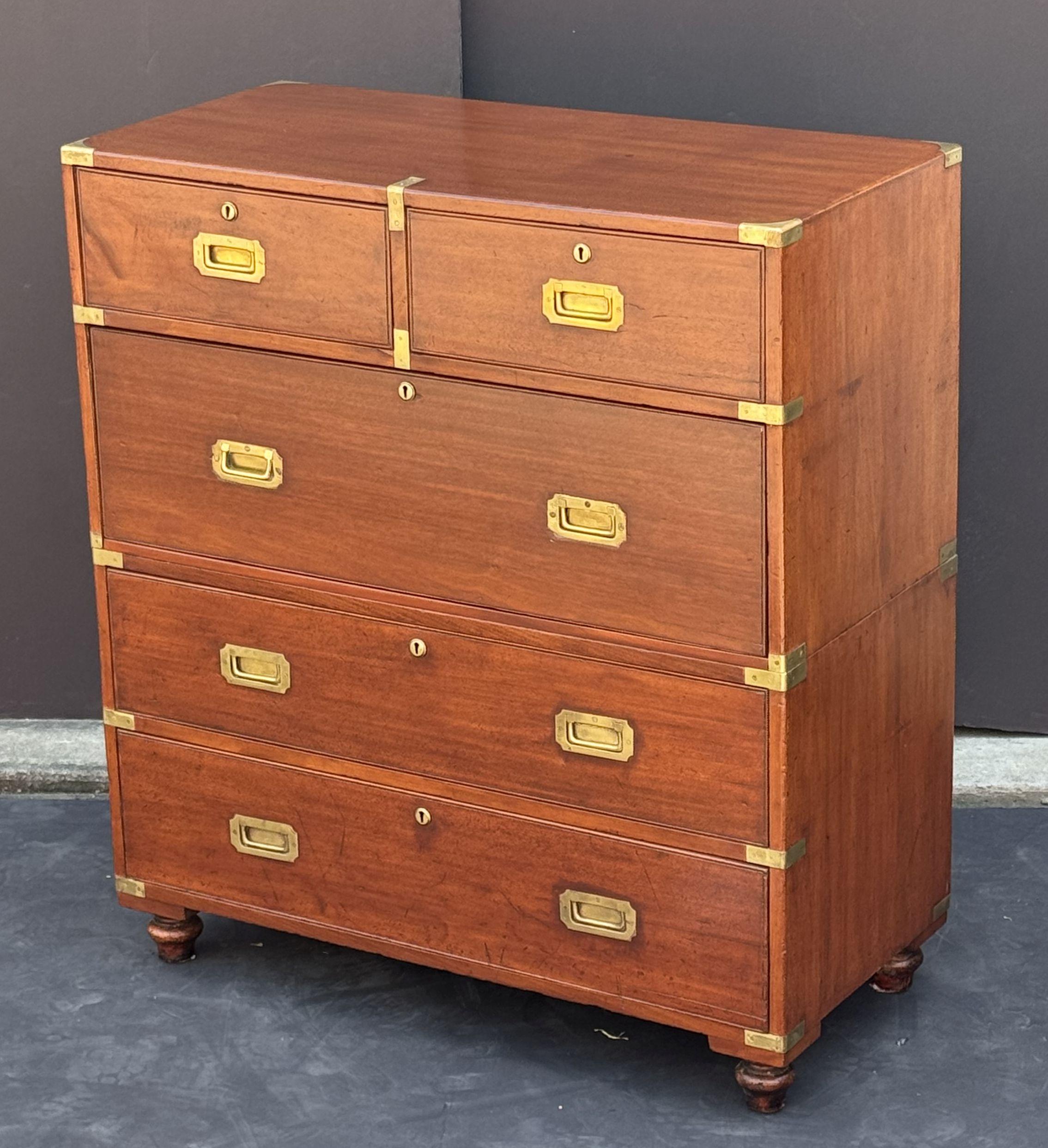 A handsome British military officer’s Campaign Ware chest of drawers or dresser, from the 19th century, featuring a patinated mahogany exterior over five drawers with brass escutcheons and recessed pulls. The brass-bound chest, in two parts - top
