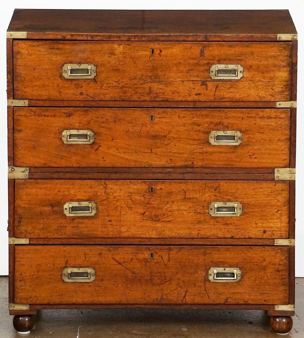 A handsome British military officer’s Campaign Ware chest of drawers or dresser, from the 19th century, featuring a patinated mahogany exterior over four drawers with brass escutcheons and recessed pulls. The brass-bound chest, in two parts - top