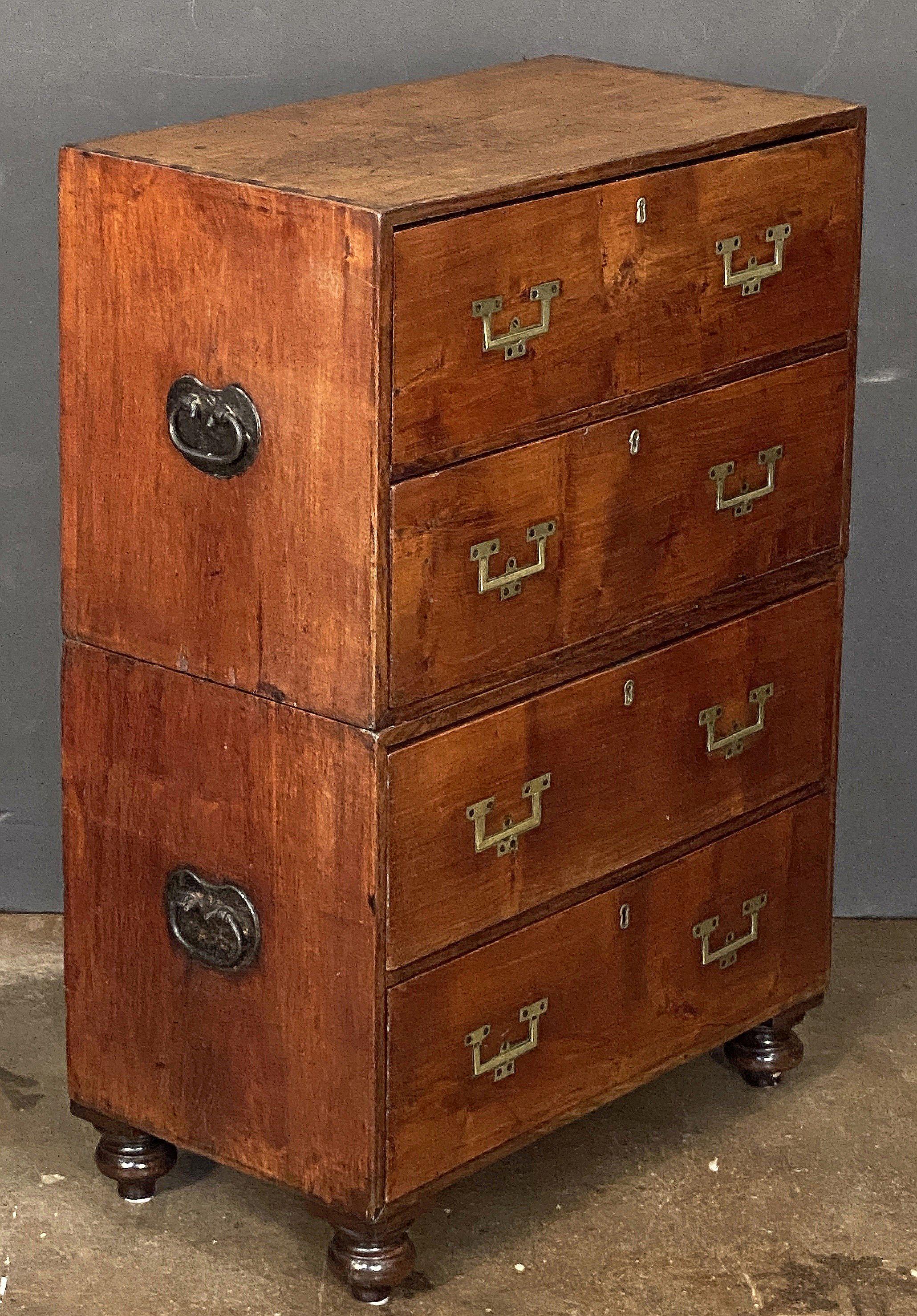 A fine and unusually diminutive British army or naval officer’s Campaign Ware chest of drawers or dresser, from the 19th century, featuring a patinated mahogany exterior with four long drawers, each with brass escutcheons and recessed pulls. 
The
