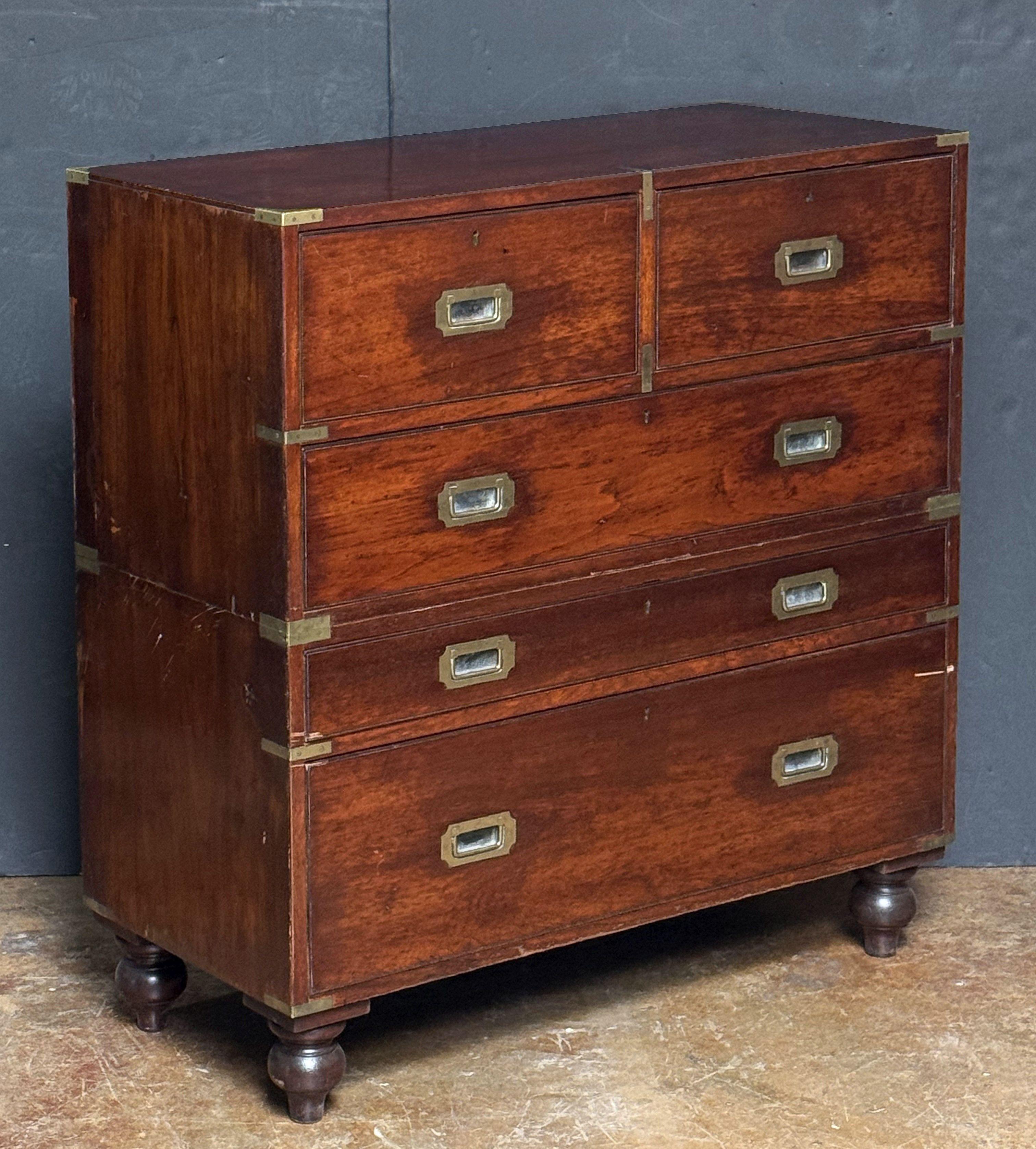A fine British military officer’s Campaign ware secretary or secretaire from the 19th century, fashioned as a chest of drawers, featuring a patinated mahogany and camphor-wood exterior, showing two short drawers over three long drawers. 
The top