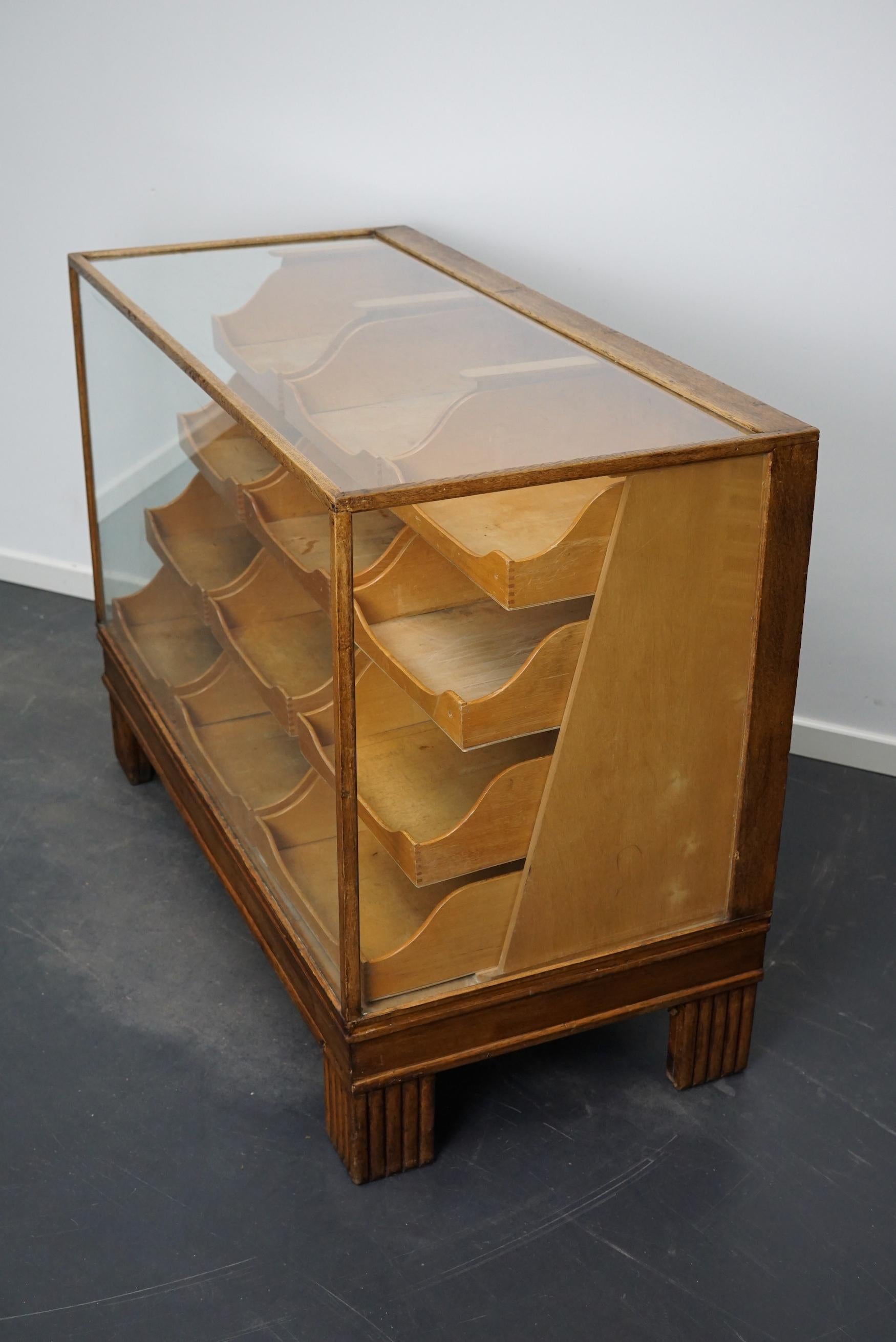 This vintage oak haberdashery shop counter dates from the 1930s and was made in England. It features a solid wooden frame, a glass casing and drawers in oak with copper handles and brass name card holders.
 