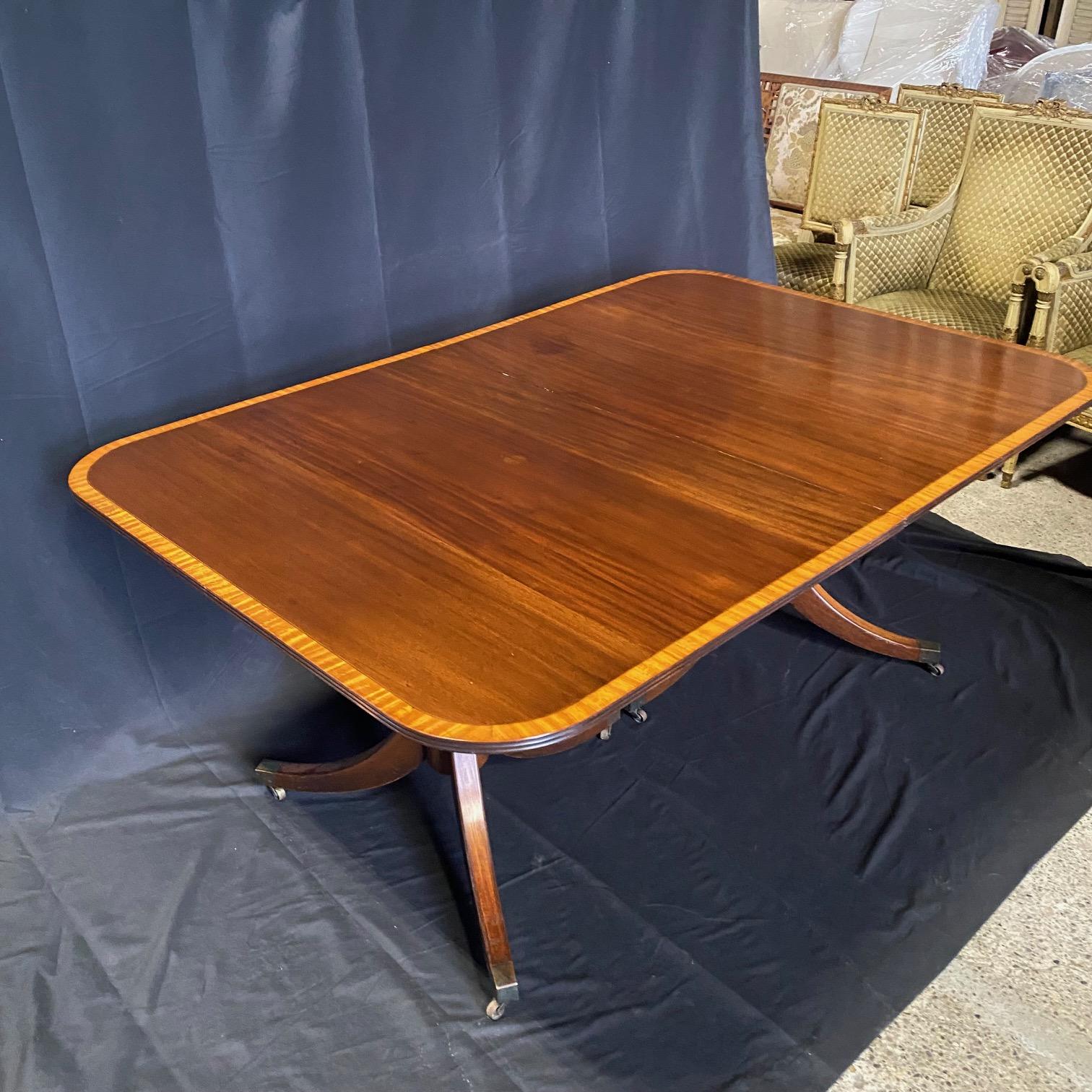 Elegant banded inlay mahogany Duncan Phyfe style dining table with two pedestals. Features an impressive satinwood banded top supported by a double pedestal mahogany base over three shapely tapered legs leading to brass capped casters. #6587
H skirt