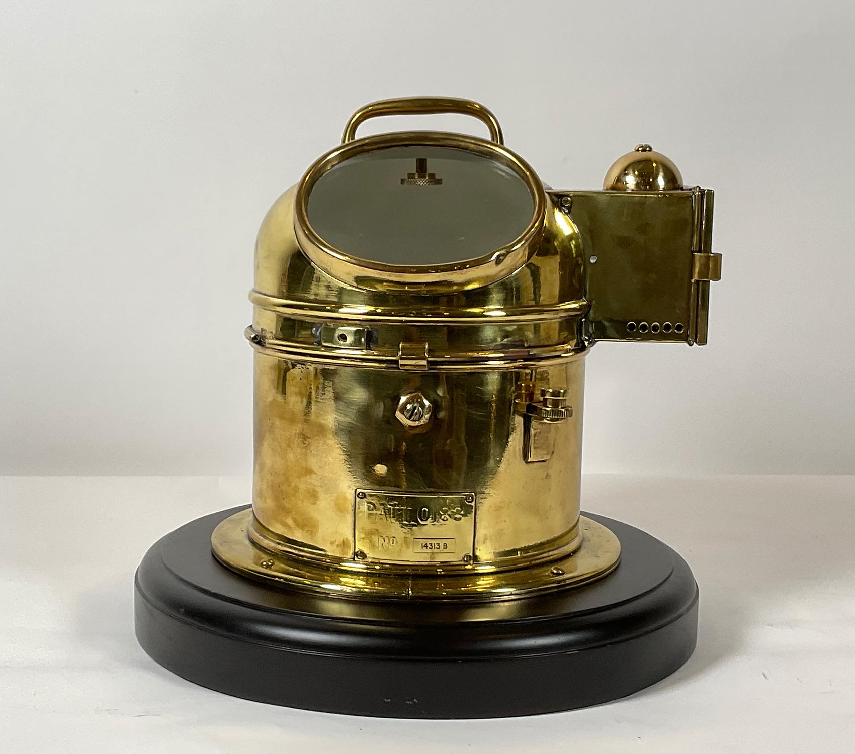 Solid brass ship’s compass on gimbal mounted into a brass binnacle housing. The nameplate reads pattern 0183, and serial number 14313-B. The compass card shows the royal crown. The binnacle is mounted onto a thick wood base with a routed edge. Solid