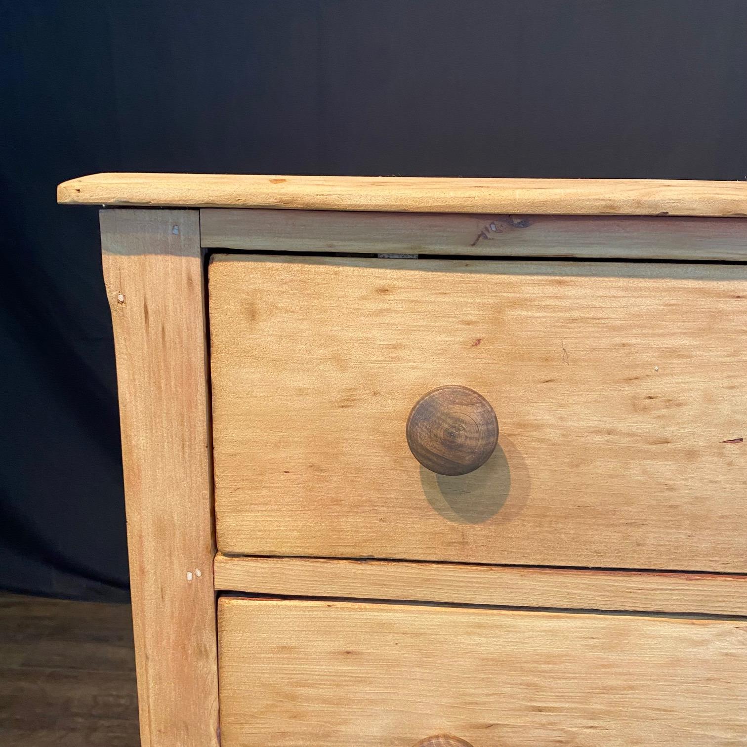 Lovely simple and primitive scrubbed pine chest of drawers, displaying an arrangement of four spacious drawers over a classic curved simple molding and a scrubbed pine wood finish. The wooden knob hardware blends nicely with the rest of the piece.