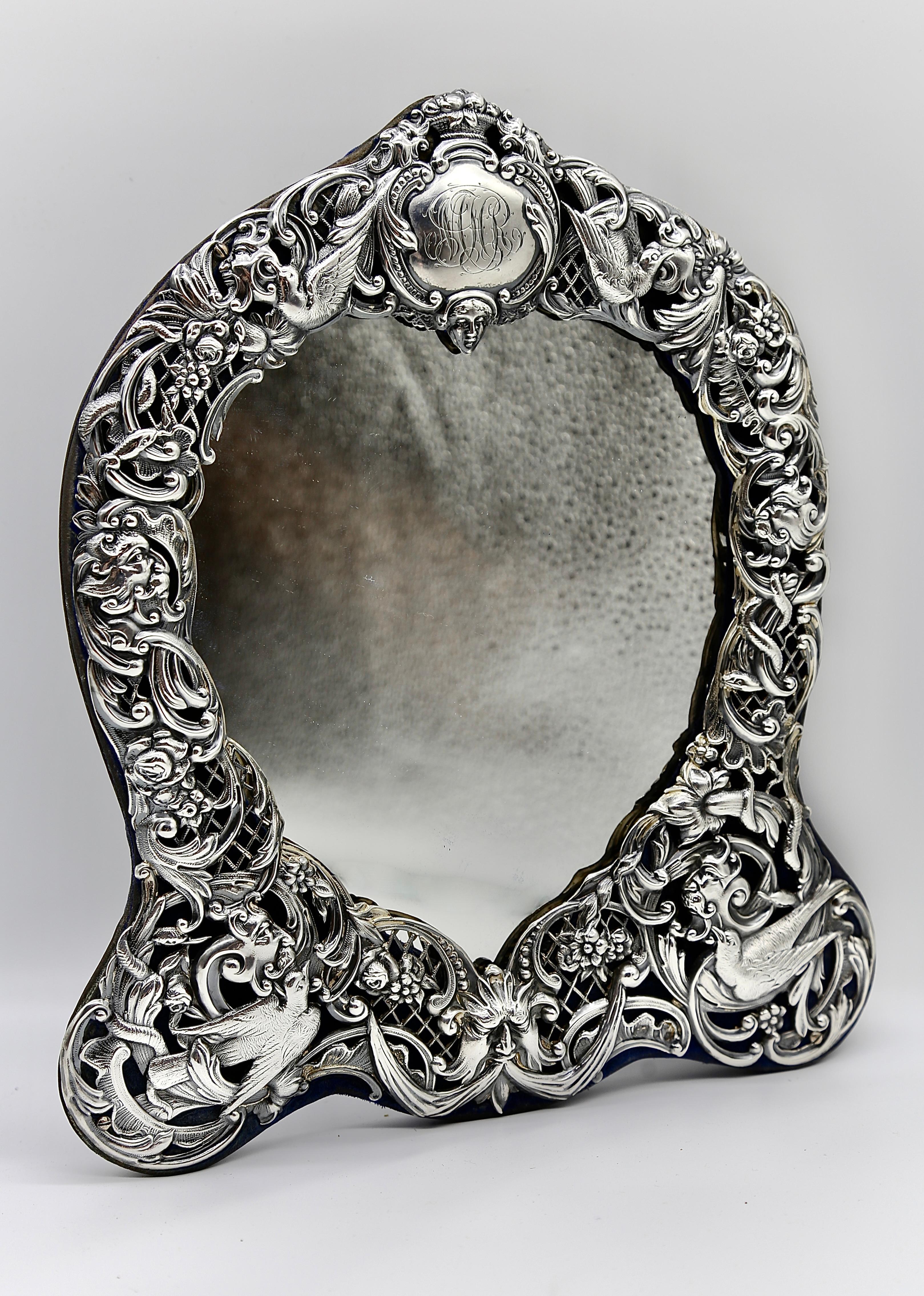 Exquisite Victorian Antique British Silver dressing table mirror in a heart shape design embossed with detailed birds and mythical faces, scrolls, flowers, foliage and lattice on a rich dark blue velvet. 

It is imposed with W.C for William Comyns,
