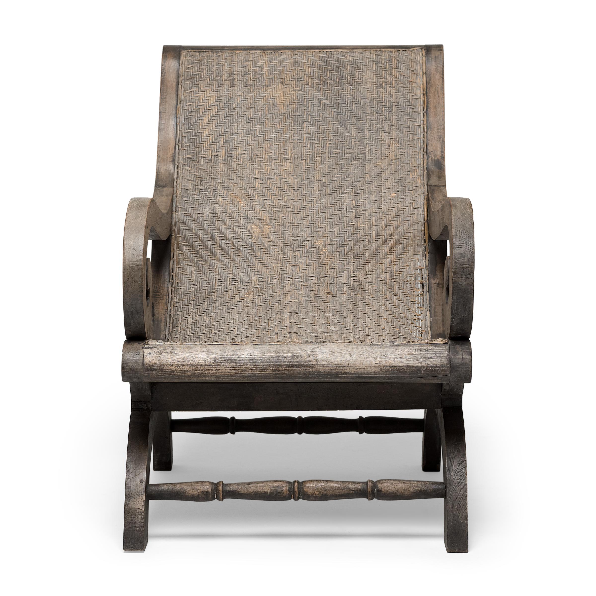 This woven rattan armchair recalls the Grand British Colonial style of the early 20th century, combining refined British interiors with natural Indian aesthetics. The plantation chair is characterized by its teak frame, deep seat and long sloping