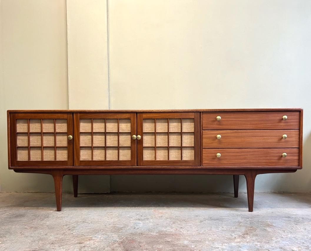 A beautiful British long teak sideboard by Younger, this would make a stylish addition to any living or work area.

The cabinet has three cupboards with a shelf to the left and a bank of four drawers to the right, all are in good order with dovetail