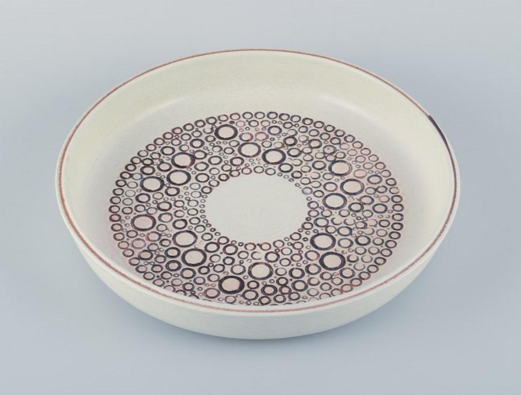 Britt-Louise Sundell (1928-2011) for Gusatvsberg, Sweden.
Large ceramic bowl in modernist design. 
Circles in brown glaze on cream-colored base. 
1960s/70s. 
Marked. 
Perfect condition. 
Dimensions: D 29.5 cm x H 5.2 cm.