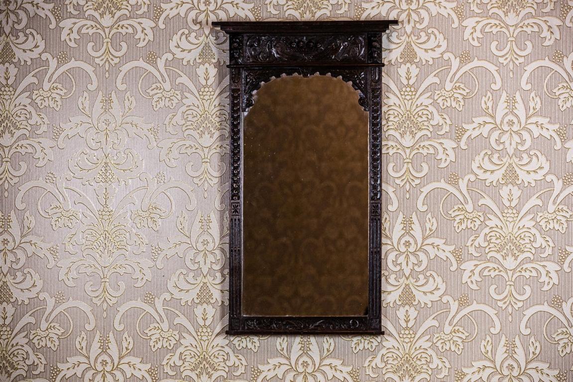 We present you a neat rectangular mirror closed in an oak frame, which is covered with carved patterns. Its stylistics refers to that of the Brittany style.
The frame ends with an arch and is topped with a simple cornice, which is supported on lion