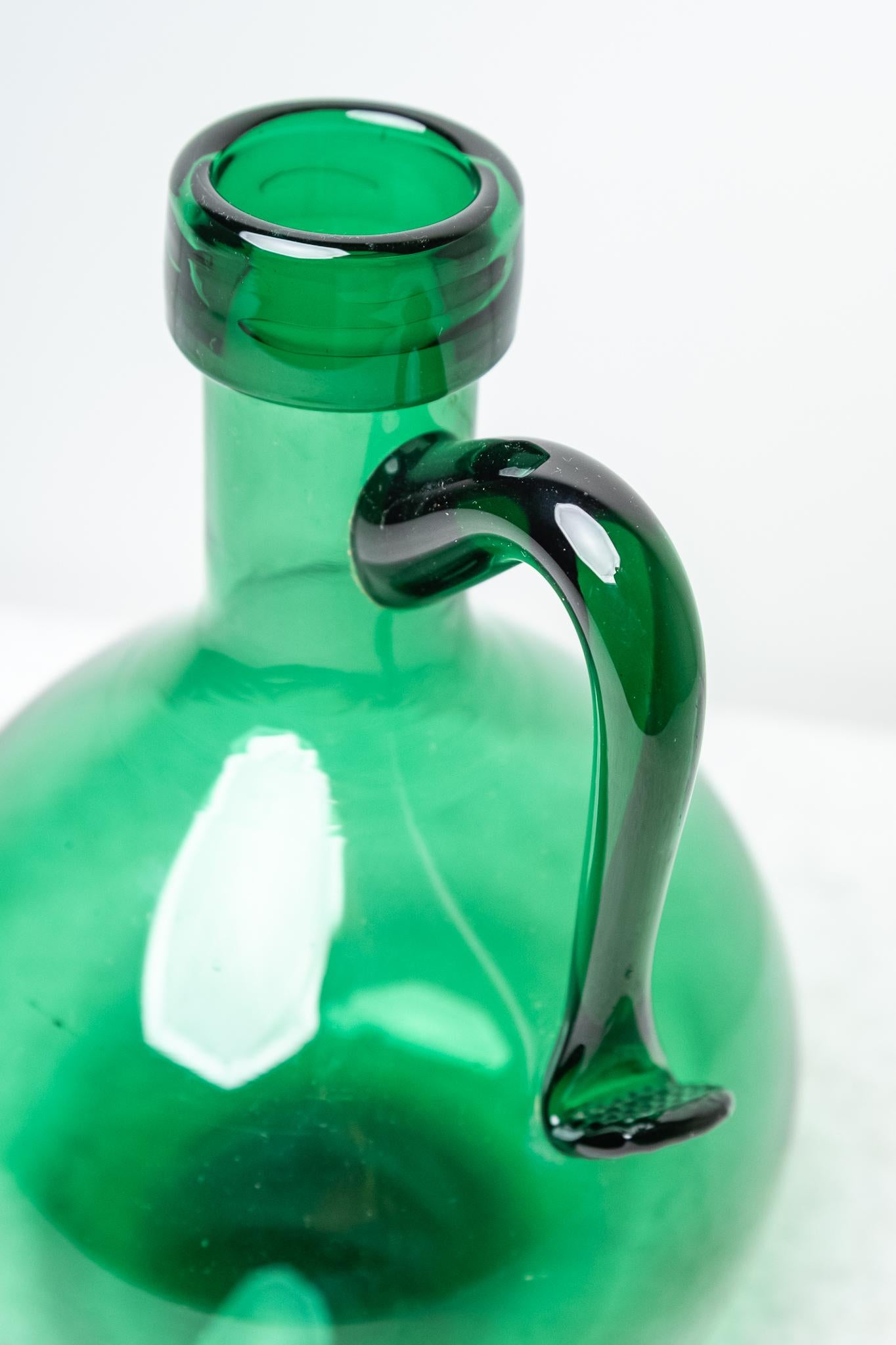 Brocca in vetro verde, Made in Italy, Anni '50. 
Particolare Brocca in vetro di spessore verde degli Anni '50, con manico che presenta delle particolari lavorazioni. Questa bottiglia oltre che da decoro può essere anche utilizzata per contenere per