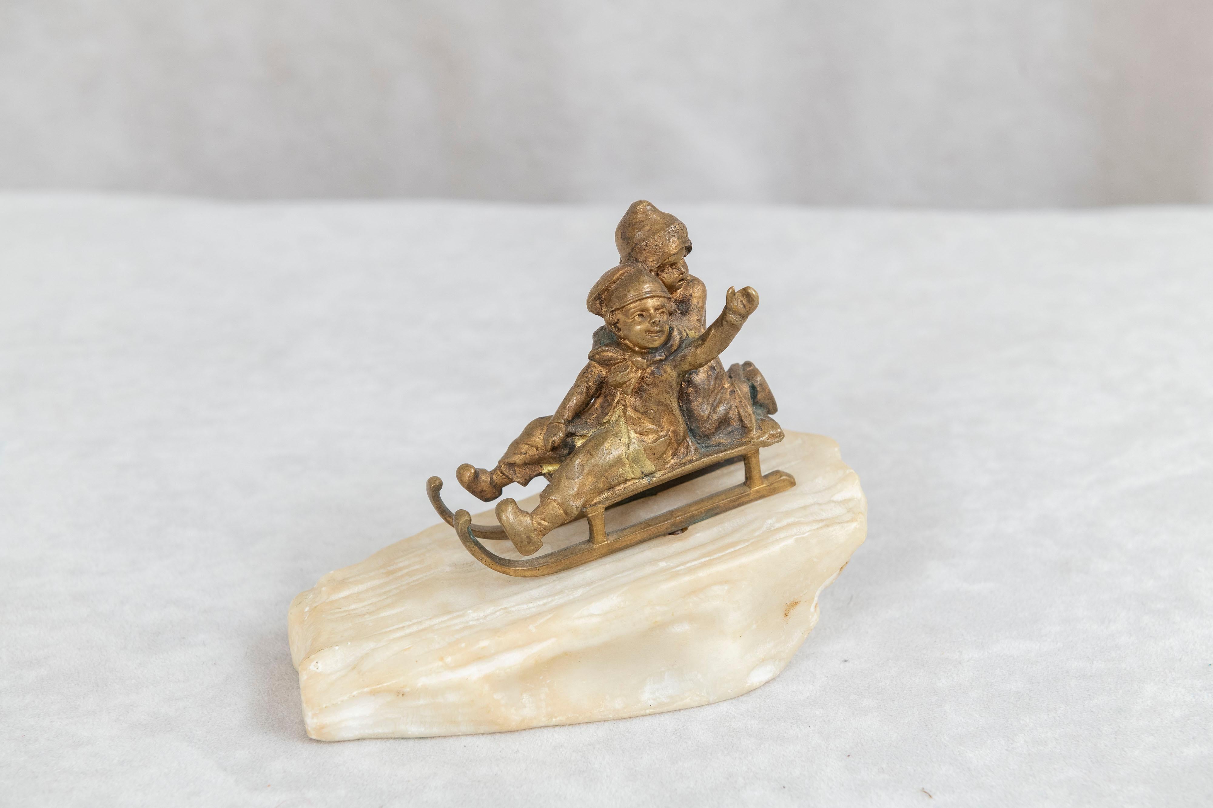 This whimsical little bronze shows 2 young children on a sled riding down a hill of snow and with one youngster waving to us. The bronze is finished in gilt and the sled is mounted on carved marble. That is marble, not alabaster, and if you ever