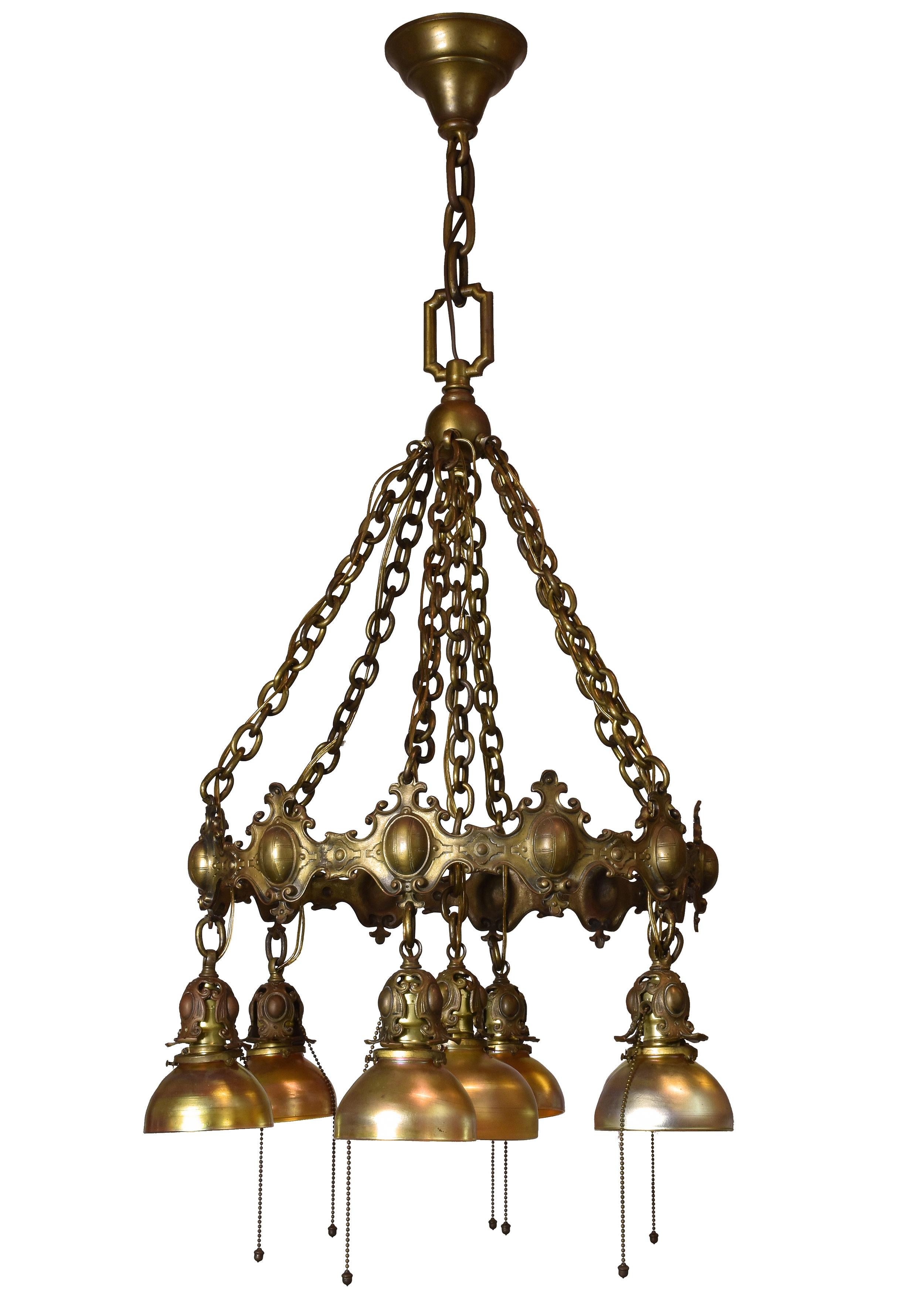 This handsome cast bronze chandelier is intricately crafted and eye-catching. The cast bronze body is made up of a shield motif with curling edges. Each of the seven shades hangs from sockets covered by leafy socket housing. The chains of the body