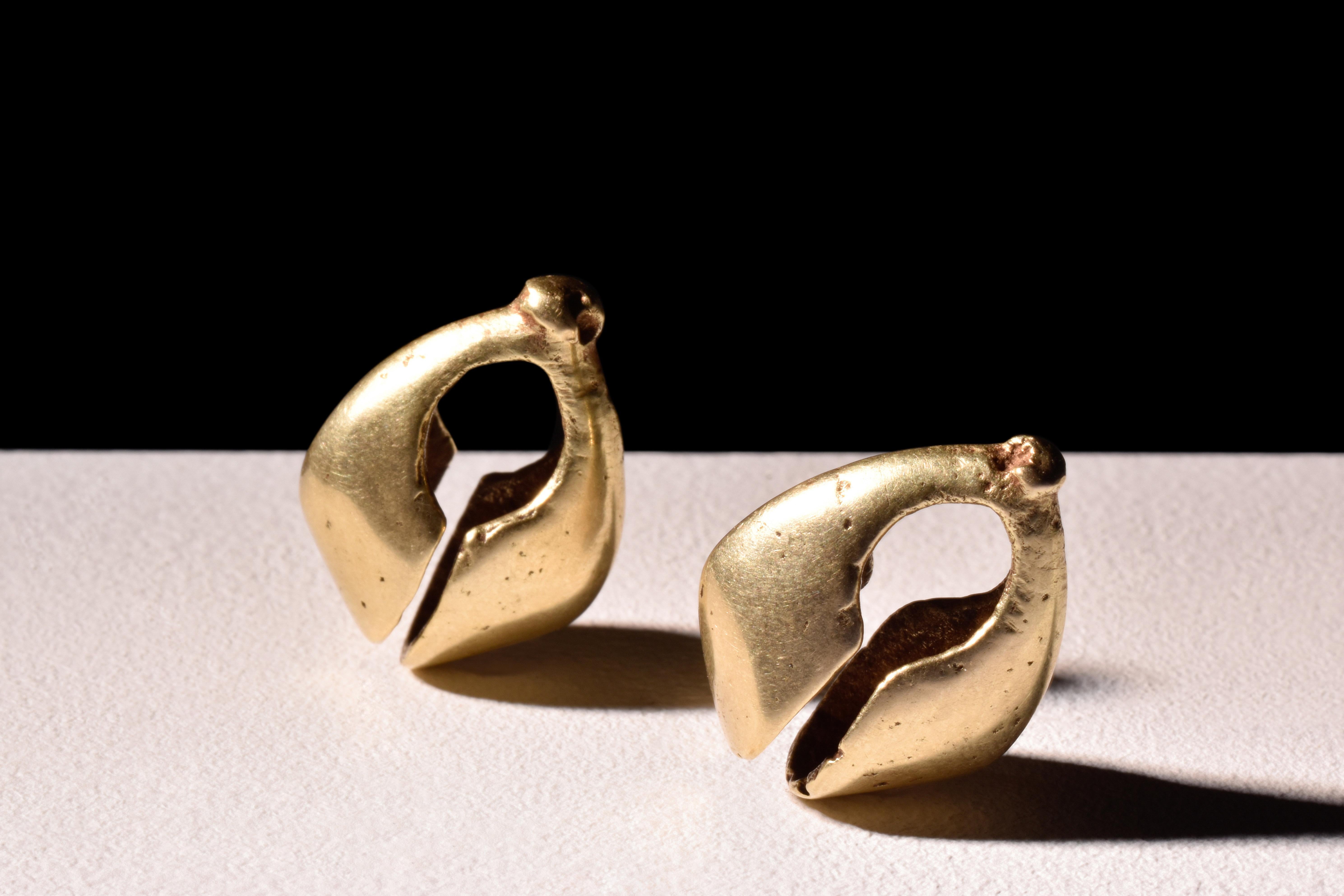A Bronze Age, matched pair of gold earrings. Each piece is characterised by hollow-formed construction. The terminals of these earrings expand gracefully, while central bulges with perforations imbue the design with an additional element of